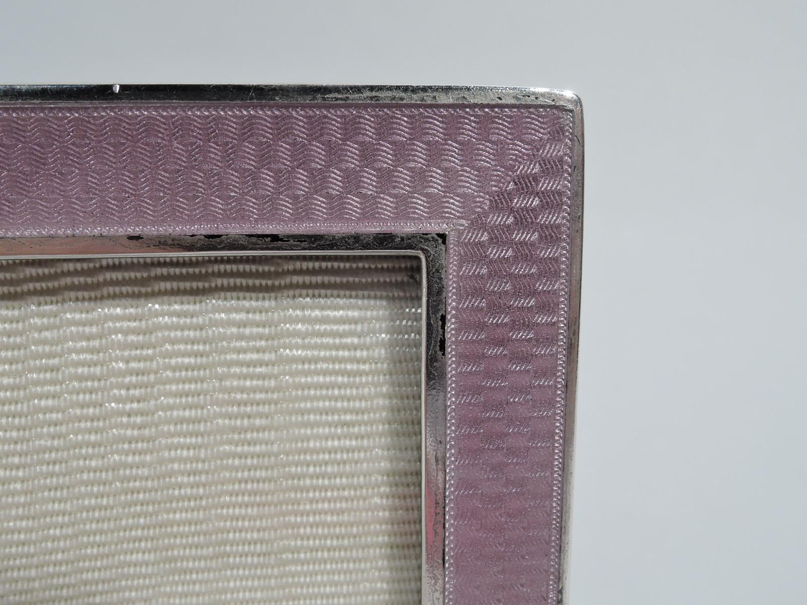 American sterling silver and enamel frame, ca 1915. Retailed by Udall & Ballou in New York. Rectangular window in flat surround with guilloche wave enamel between silver borders; sides silver. Enamel is pink. With glass, silk lining, and wood