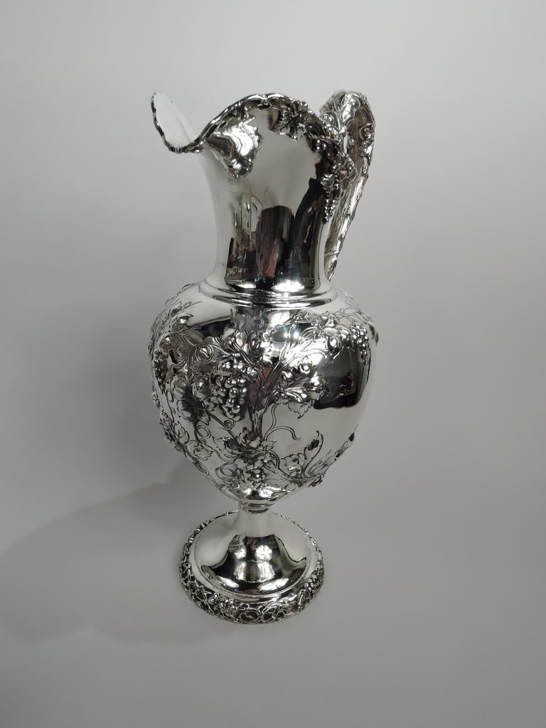 Victorian sterling silver pitcher. Made by Dominick & Haff in New York in 1894. Ovoid body with chased fruiting grapevines forming 2 irregular frames (vacant). Helmet mouth and raised and round foot with same applied to rims. High-looping