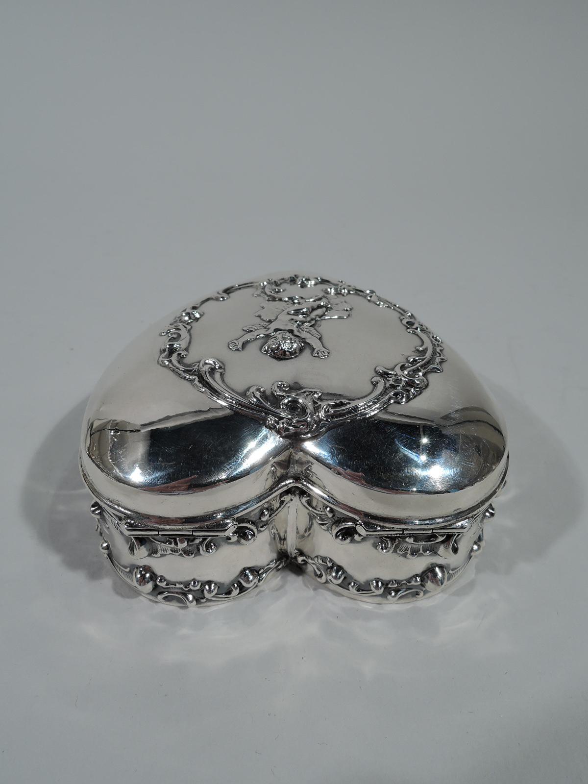 Romantic heart-form sterling silver jewelry box. Straight sides and hinged and raised cover. Applied ornament. Sides have scrolls and cover has gleeful arms-raised-high cupid in scrolled wreath. Box interior velvet lined. Cover interior gilt-washed.