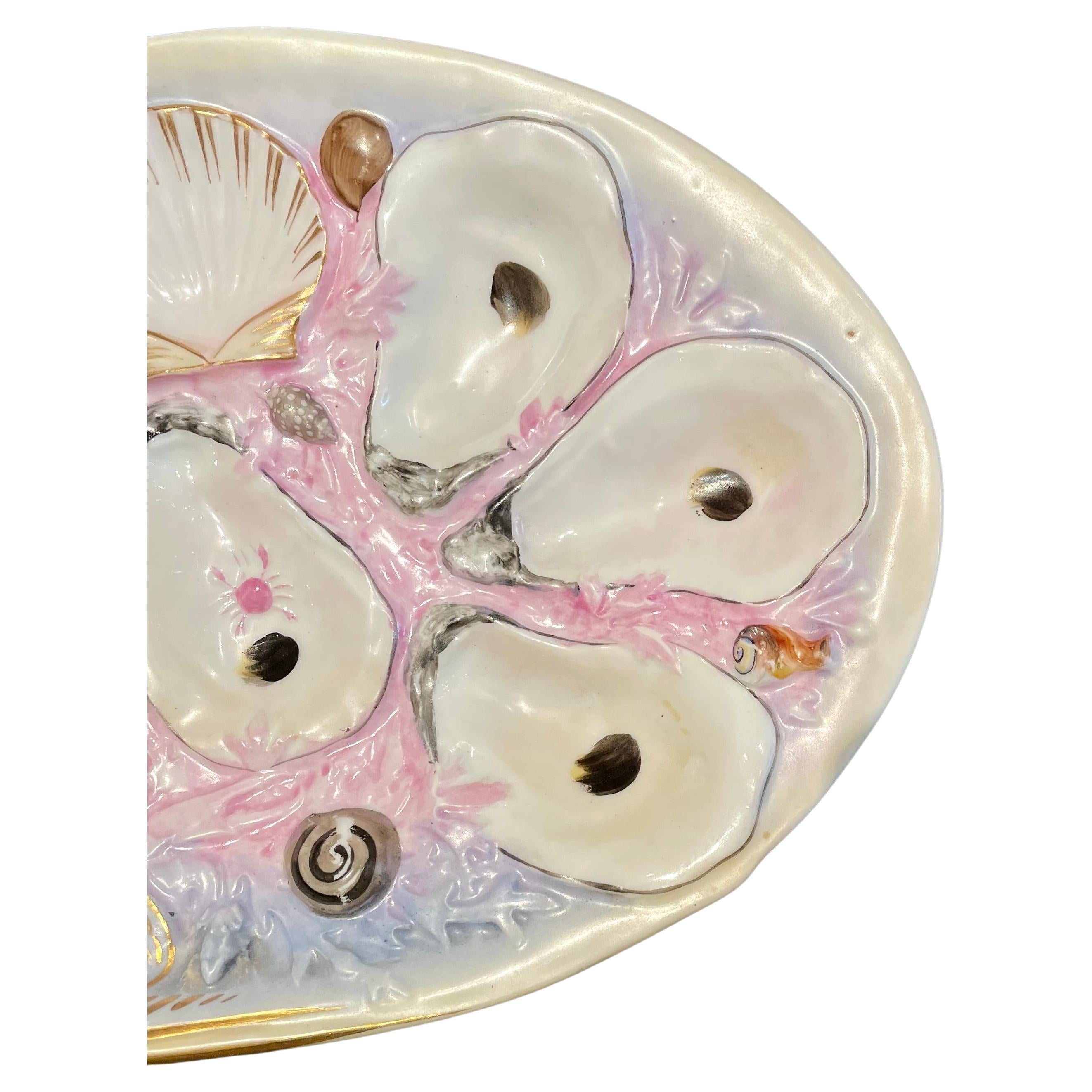 Ancienne assiette à huîtres en porcelaine rose en forme de palourde de Union Porcelain Works, vers les années 1880.
D'une taille inhabituelle pour UPW, il est façonné et peint à la main en rose et violet avec des détails de la vie marine.  
