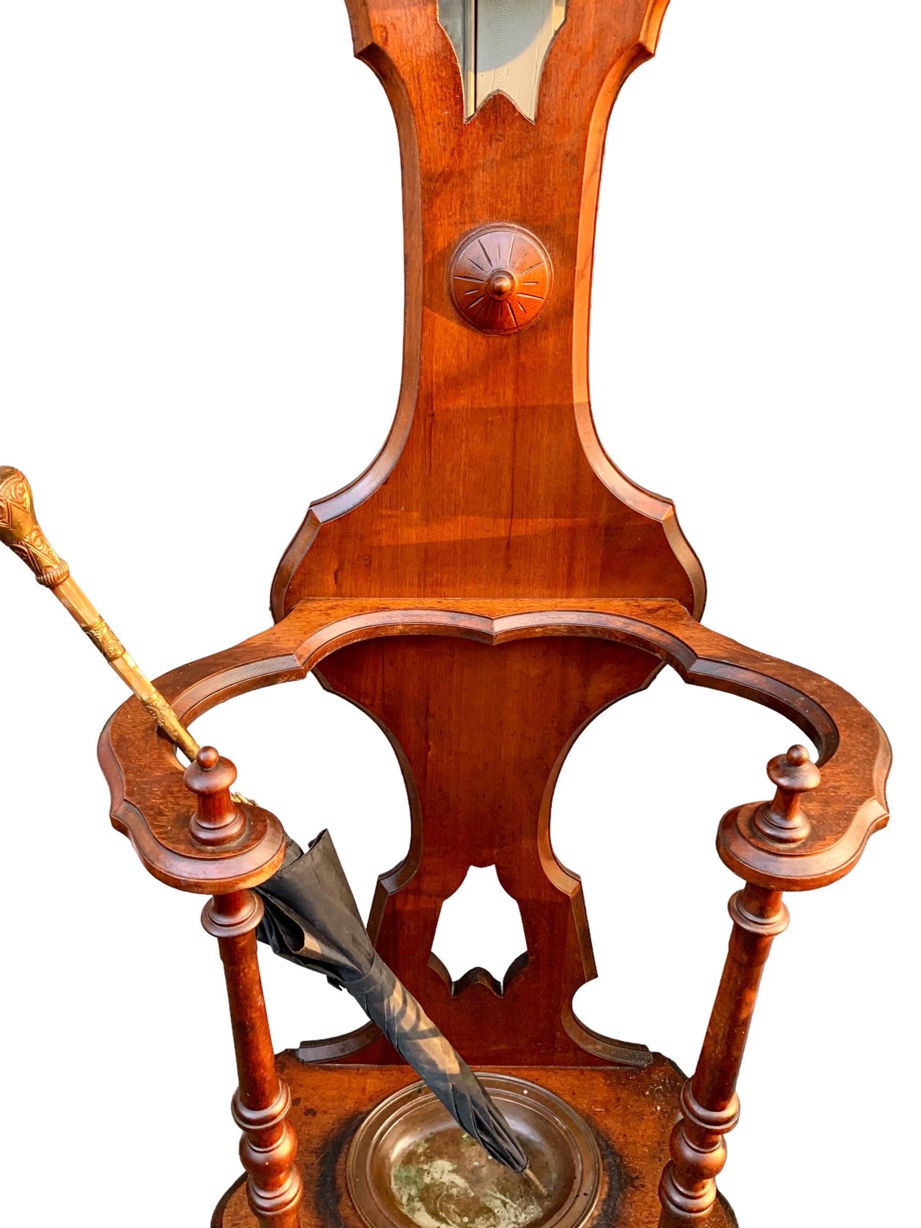 An antique American Victorian carved walnut hall stand, late 19th c., having a lovely arched top over three wooden coat pegs and a central arched mirror, flanked by two coat pegs, above two lower coat pegs and an open umbrella stand with it's