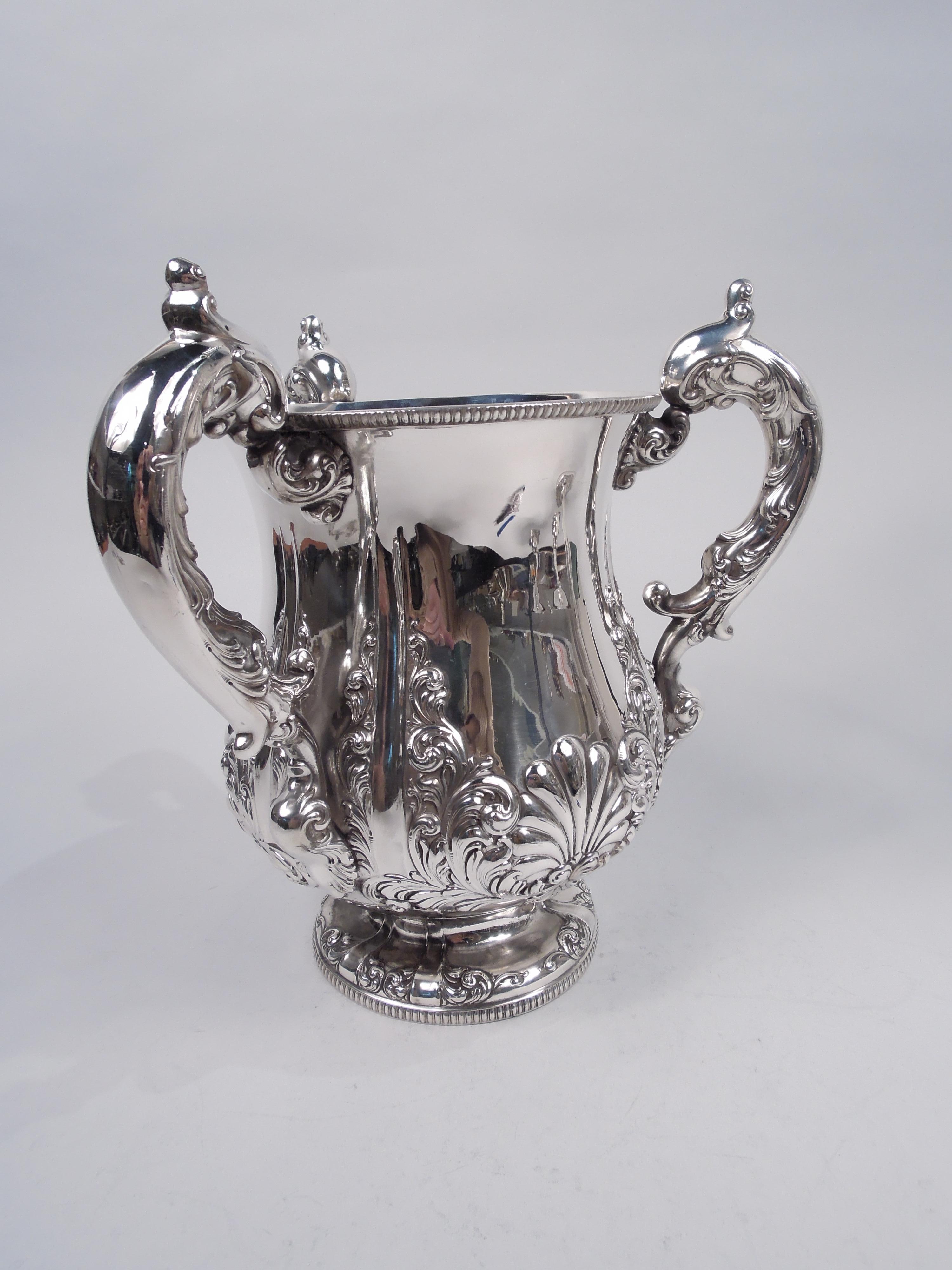 Victorian Classical sterling silver loving cup, ca 1890. Baluster bowl with flared rim and raised foot. High-looping capped double-scroll handles. Exuberant embossed and cast ornament with scrolling leaves and scallop shells contained by fluted