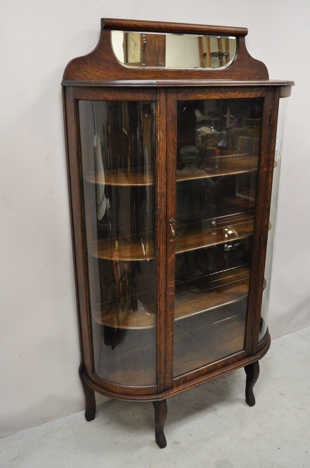 Antique American Victorian oak wood curved glass china display cabinet. Item features a curved glass sides, beveled glass mirror backsplash, beautiful wood grain, 1 glass swing door, 3 wooden shelves, very nice antique item. circa Early 1900s.