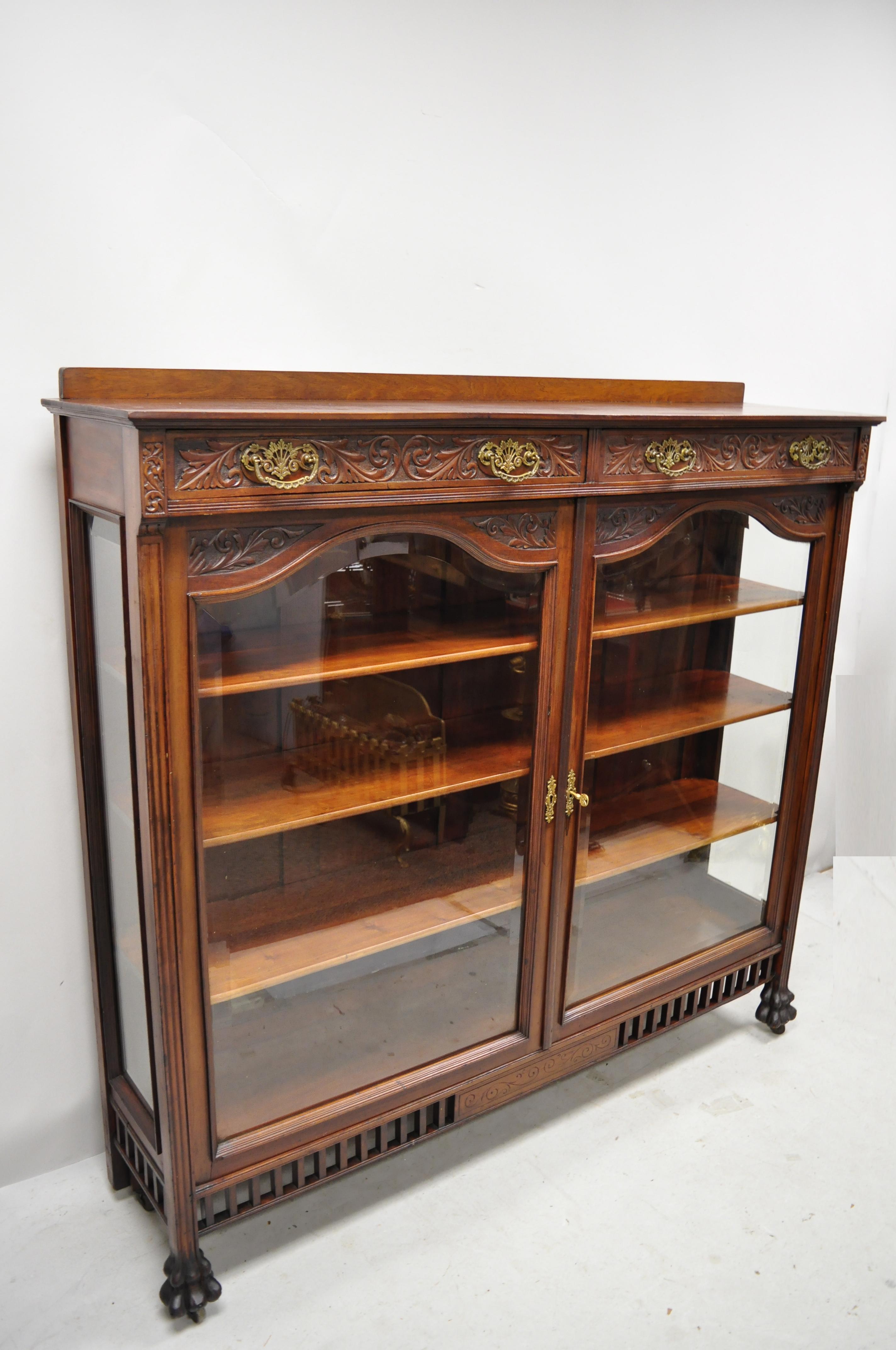 Antique American Victorian paw feet carved mahogany China cabinet bookcase curio with 2 drawers. Item features beautiful wood grain, nicely carved details, 2 beveled glass swing doors, 2 dovetailed drawers, 3 wooden shelves, carved paw feet, very