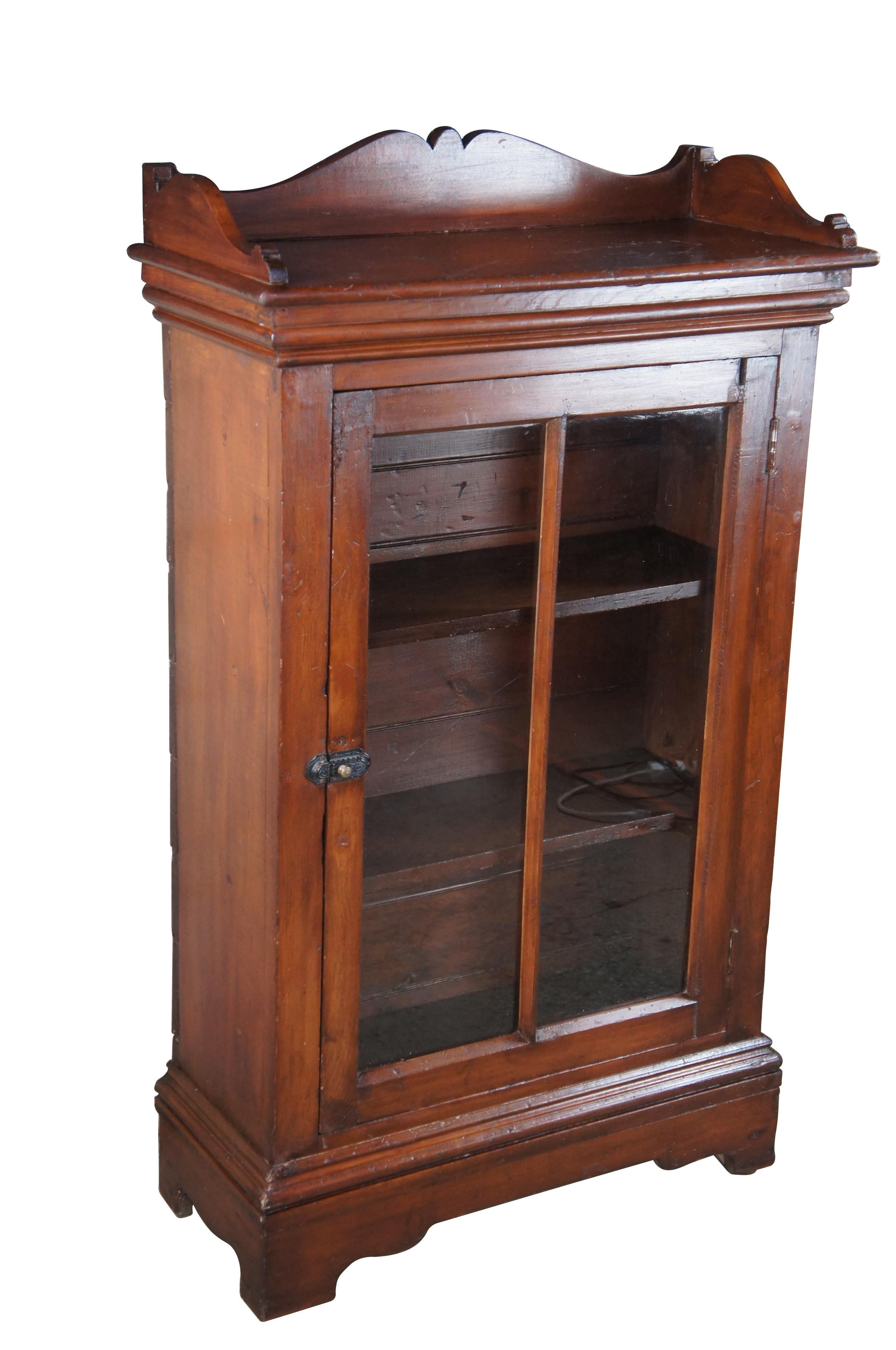 19th Century American Victorian curio / display cabinet.  Features a rectangular form made from pine with serpentine backsplash.  A central door opens via metal latch to two interior shelves.  Back is sided with hand cut nails.  

Dimensions:
33