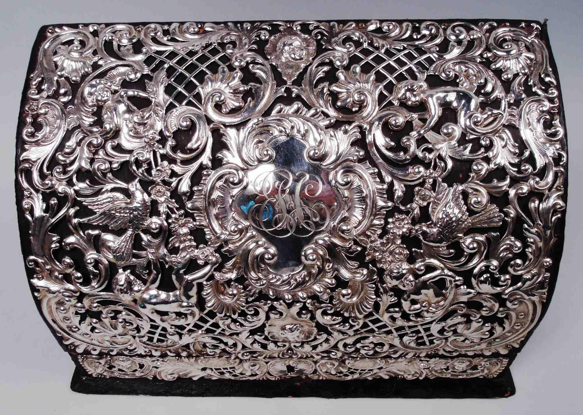 Buzón victoriano americano rococó de plata de ley y cuero, hacia 1880. Base rectangular con lados rectos y tapa abatible inclinada con frente curvo. Adorno abierto de plata aplicada en forma de palomas arrulladoras, caritas de bebé de mejillas