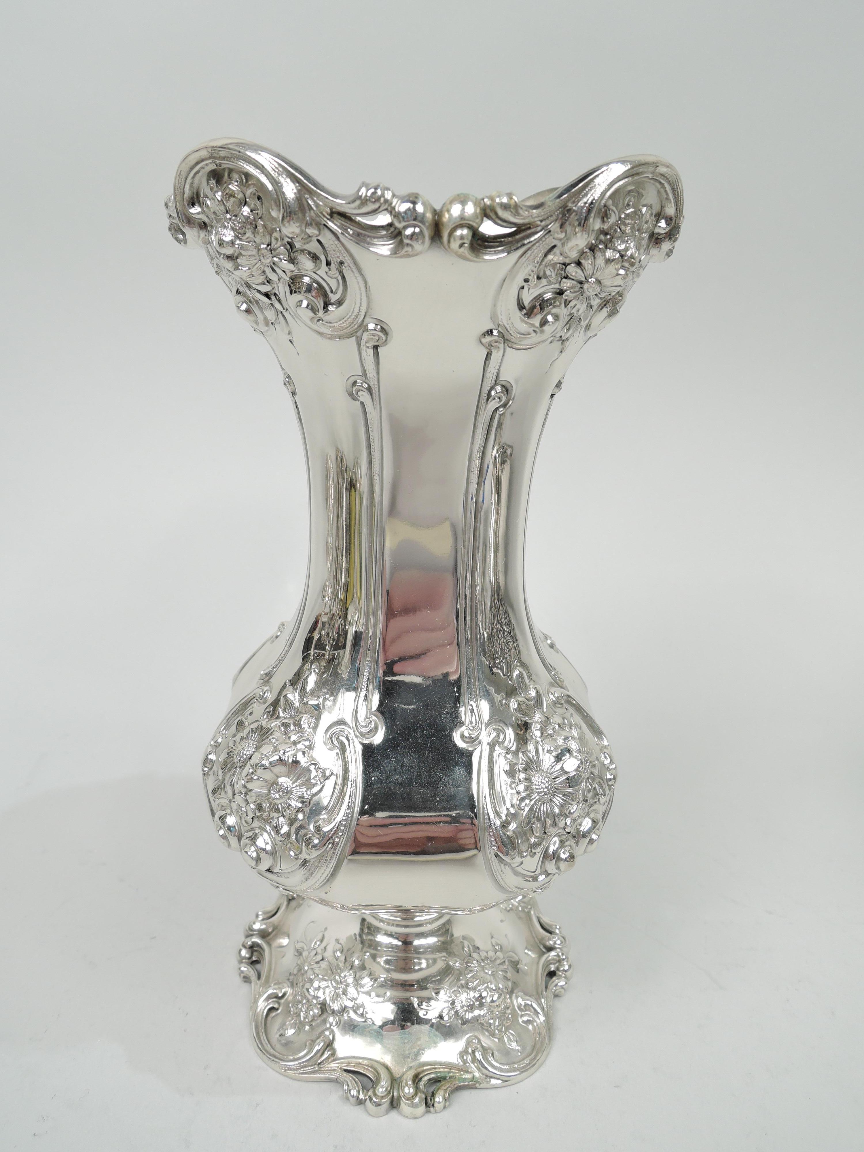 Victorian sterling silver vase. Made by Redlich in New York, circa 1900. Wide quadrilateral baluster with flared rim and domed foot. Chased scrolled frames inset with flowers at rim and bowl corners. Raised flower clusters on foot. Rims have applied
