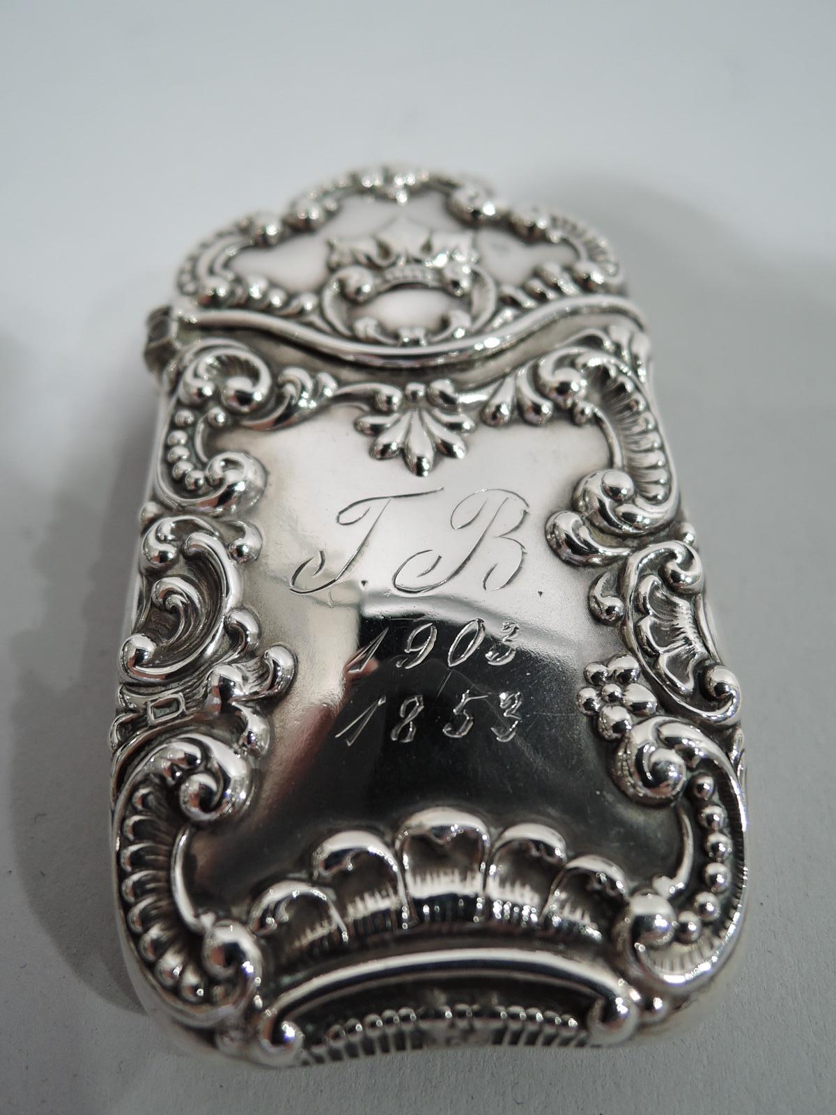 Turn of the century American Victorian sterling silver vesta case. Rectilinear with gently curved sides and shaped and hinged cover. Double-sided ornament with applied scrolls and shells; at top a regal crown. One side engraved with script initials