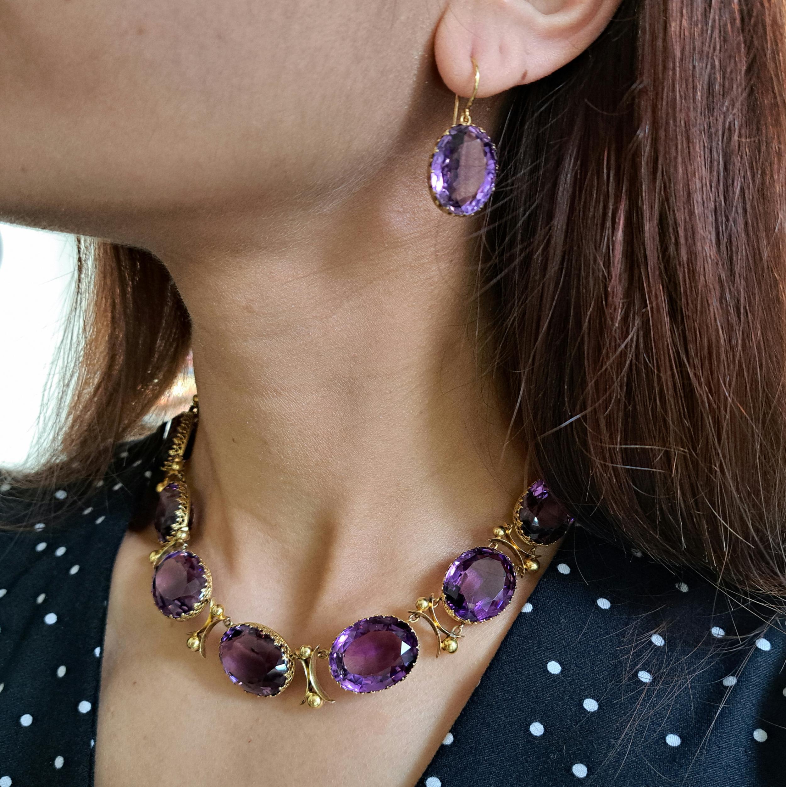 An antique amethyst and gold riviére necklace and earrings suite, with large, oval faceted, graduated amethysts, in open backed decorative, trefoil design, gallery strip bezel settings, with curved cross and ball links between the amethysts, with a