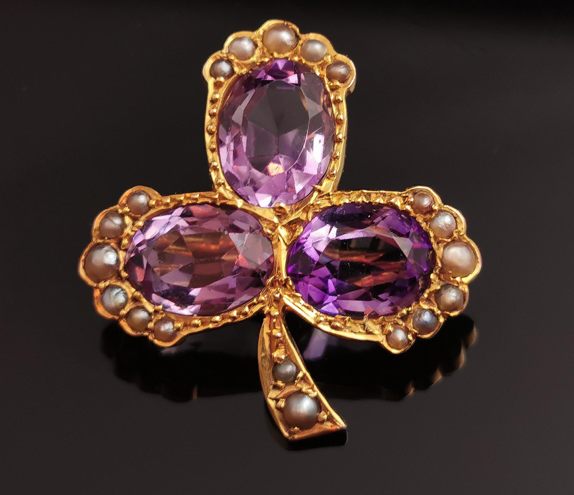 An impeccable antique Amethyst and pearl Shamrock brooch.

Rich 15kt gold gives a warm glow to this piece and the brooch has been designed as a three leaf shamrock or clover leaf.

Each leaf is set with the most beautiful rich purple Amethyst, oval