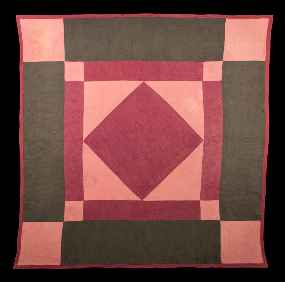 A large Amish quilt of center diamond pattern made from a blush rose red and pine green chambray cotton and wool blend. The center diamond in the square pattern is supplemented with four smaller square corners, rendering its bold iconic aesthetic.