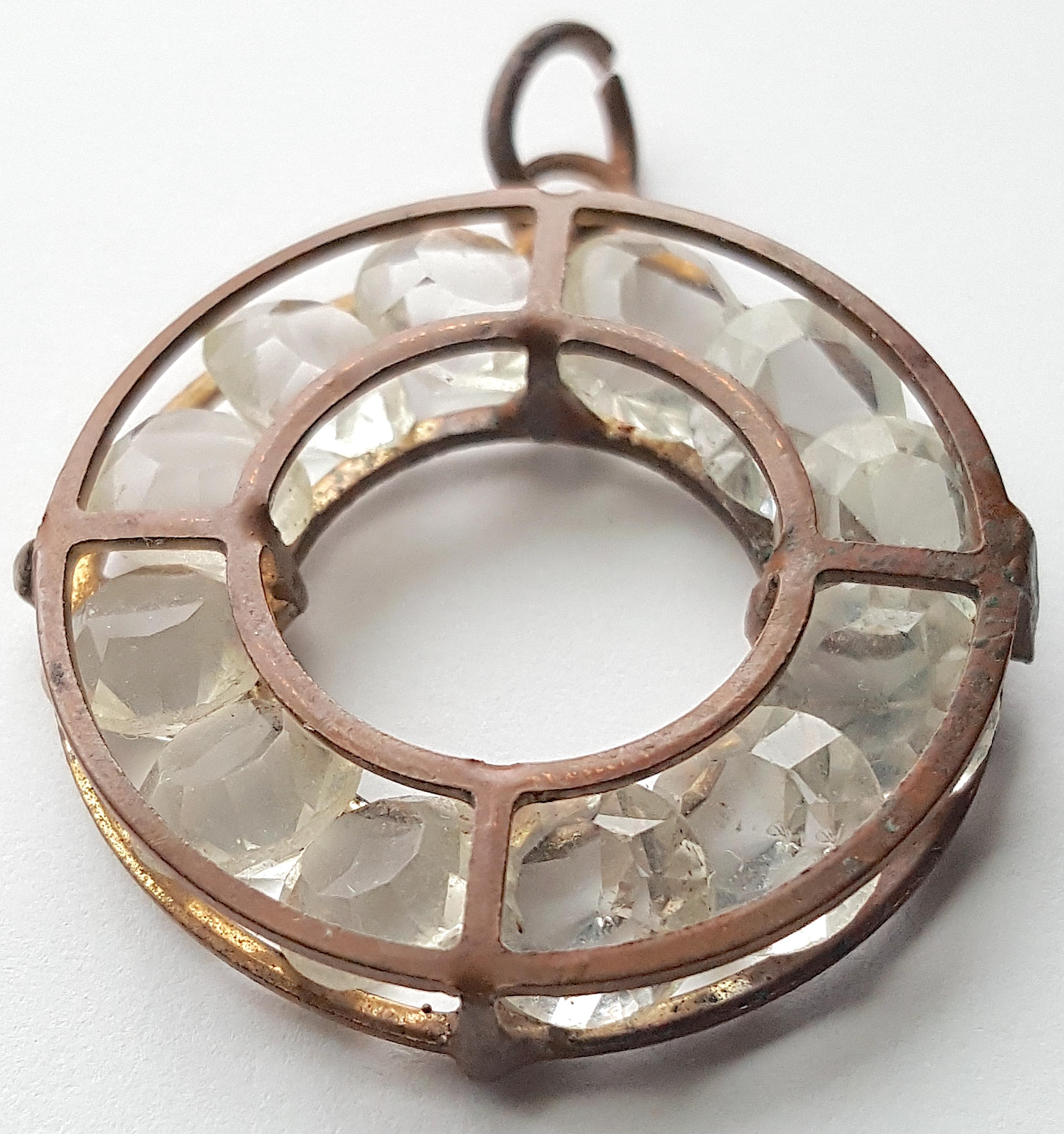 This antique amuletic bronze framed pendant cages a dozen single-cut rock crystals that each feature a table-cut decagon crown, deep pavilion, 21 facets, uncut girdle, and 7mm diameter. They are tightly set within four linked rings to overlap at the