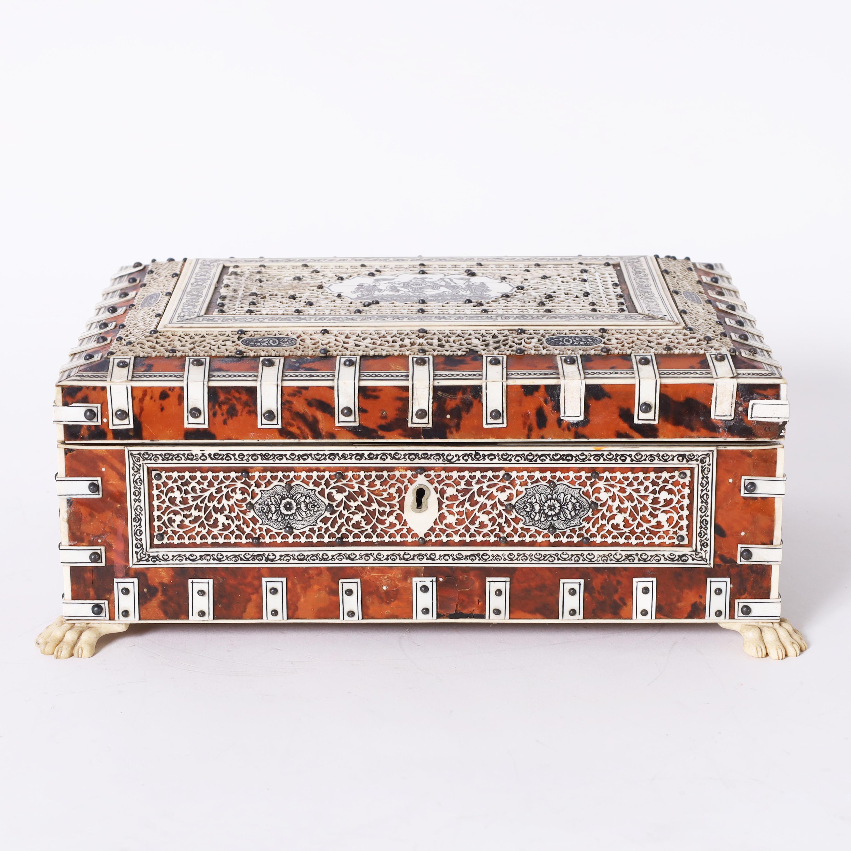 Impresionante caja antigua angloindia con tapa, hecha a mano con maderas duras autóctonas, revestida de concha de tortuga y decorada con elaborados diseños de encaje de hueso, con un medallón central grabado y pintado y patas de garra. El interior