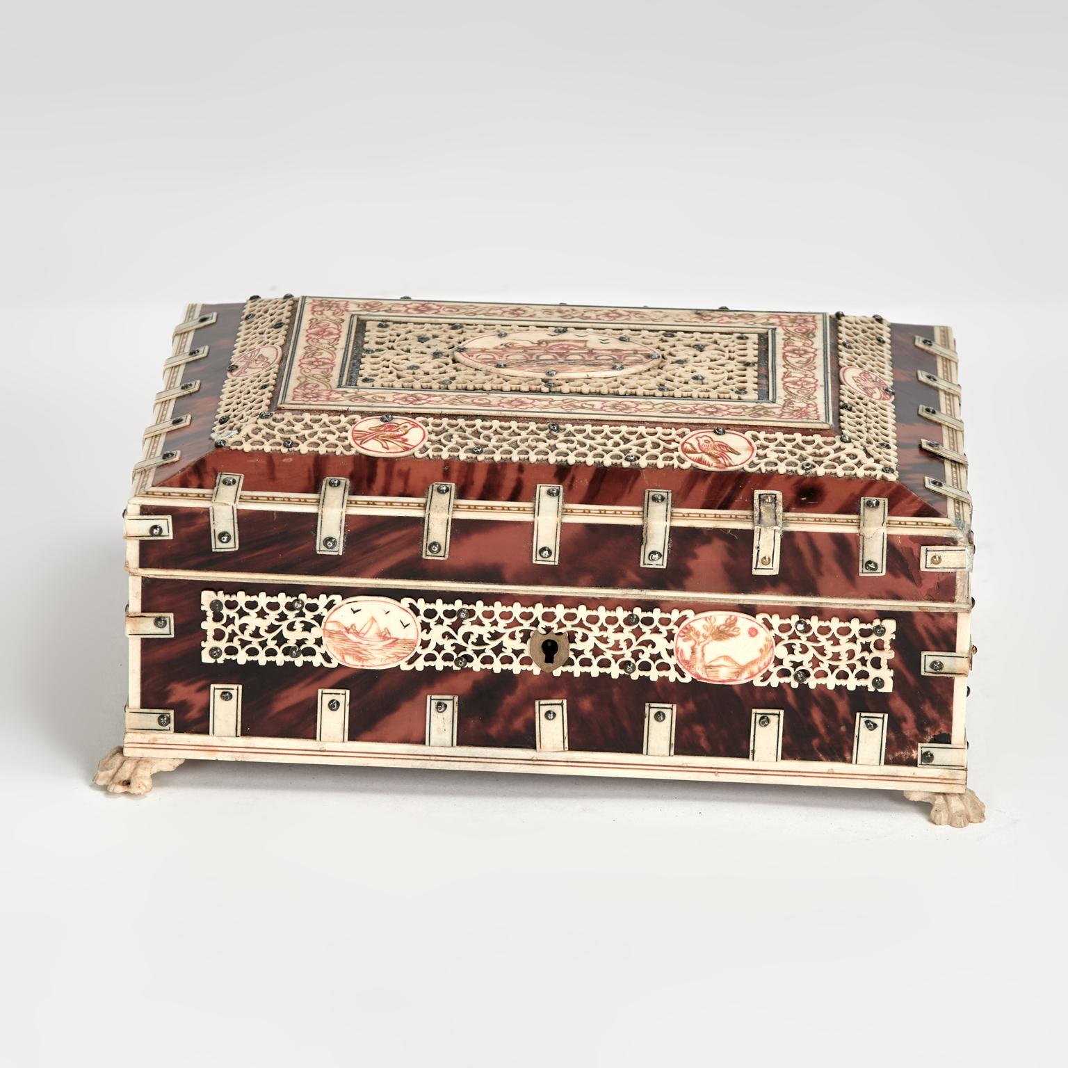 Lofty antique British colonial lidded box handcrafted in indigenous hardwood clad in tortoise shell and decorated with intricate bone designs, featuring an etched and painted center medallion and carved paw feet. The interior is lined in felt and
