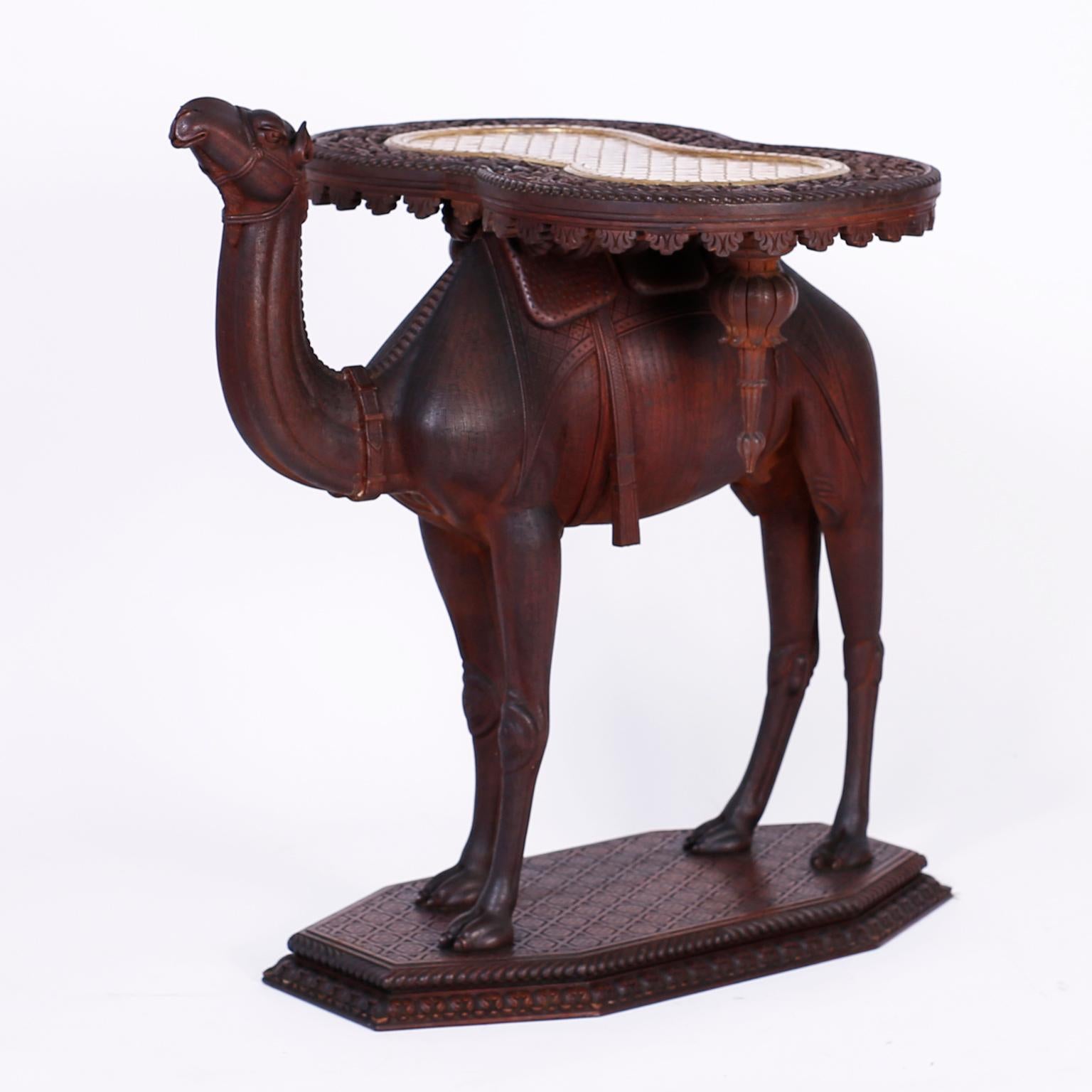 Antique Anglo-Indian British colonial occasional table or stand crafted in mahogany with an elaborately carved removable top highlighted with an inset hand hammered brass tray. The carved mahogany camel base has an enchanting familiar expression and