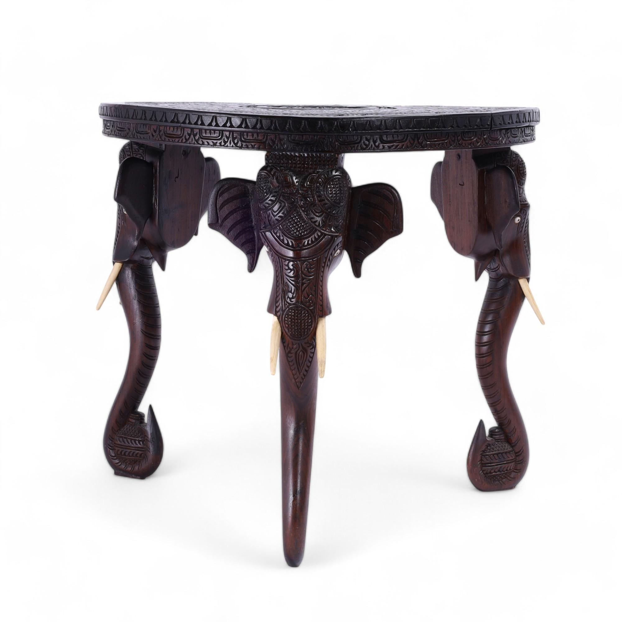Magnifique table d'appoint anglo-indienne fabriquée à la main en acajou avec un plateau rond comportant un médaillon central figuratif à l'intérieur de bordures florales élaborées, sur trois pieds sculptés en tête d'éléphant avec des yeux et des