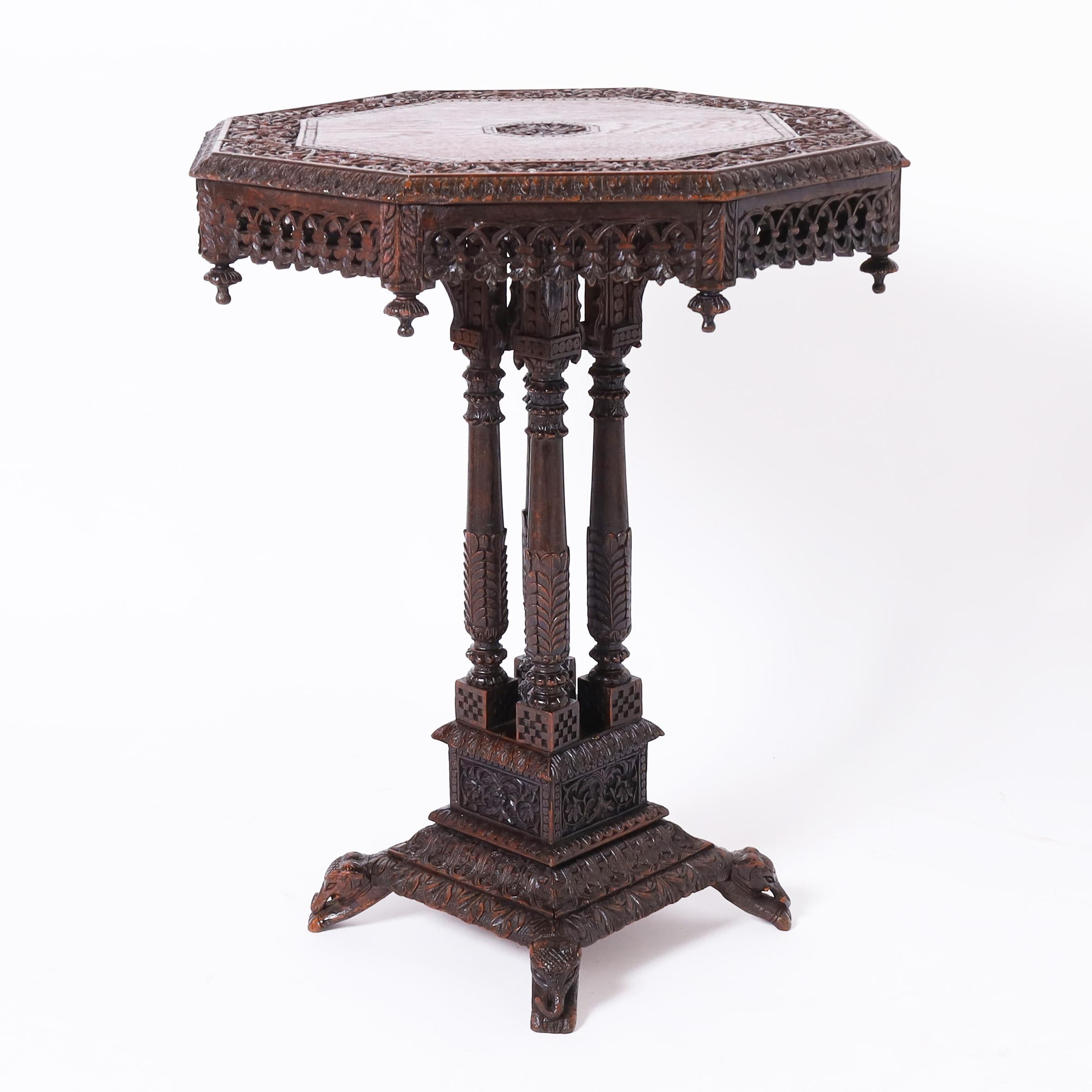 Standout antique Anglo Indian table or stand handcrafted in mahogany, having an octagon top with a carved floral center medallion, floral border and carved skirt with finials, over four columns on a two tiered carved base with elephant feet.