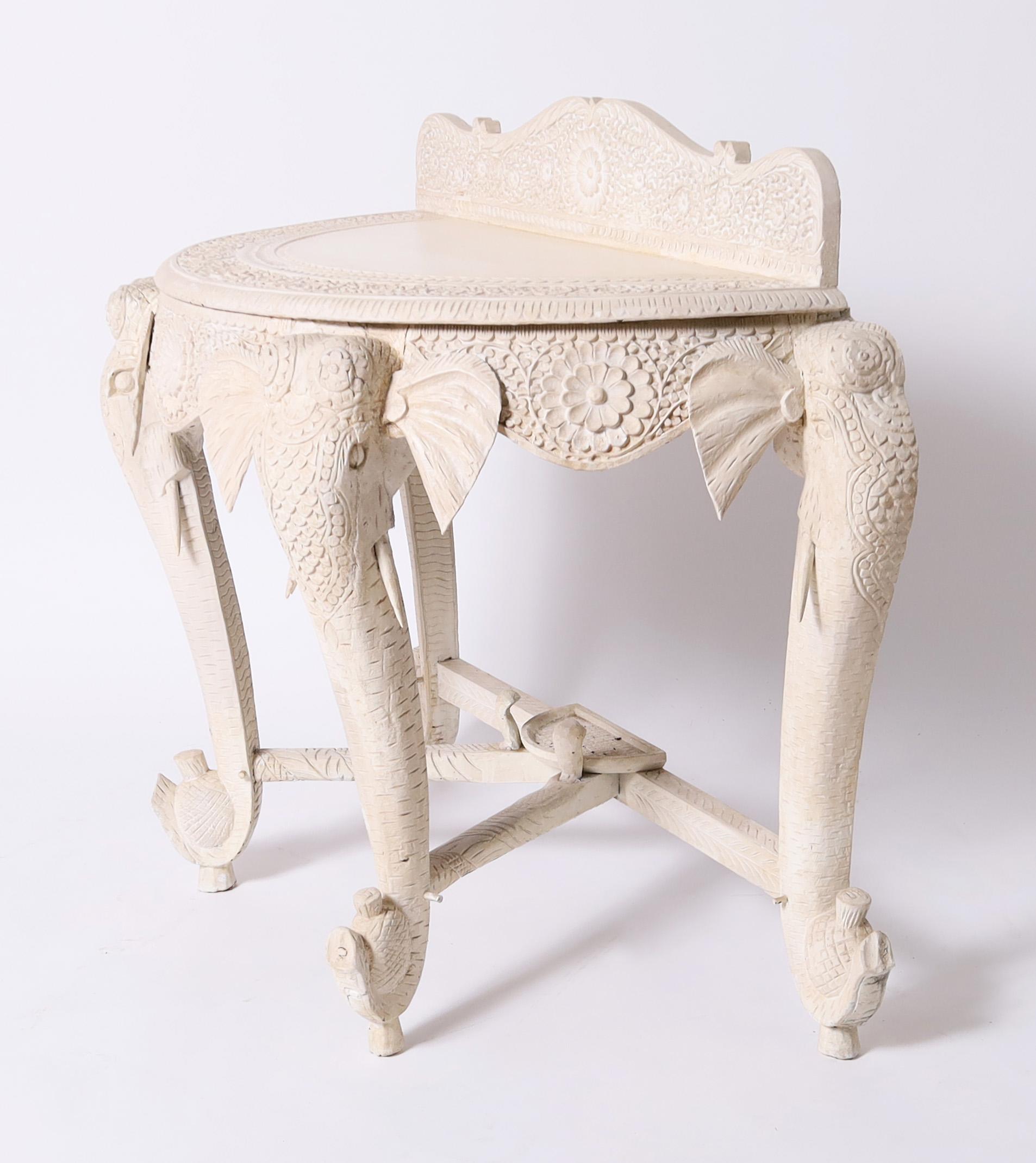 Impressive 19th Century Anglo Indian console table handcrafted in teak wood in a demi-lune form featuring a floral carved gallery and shirt, four carved elephant head legs with pineapples and a chic off white finish.