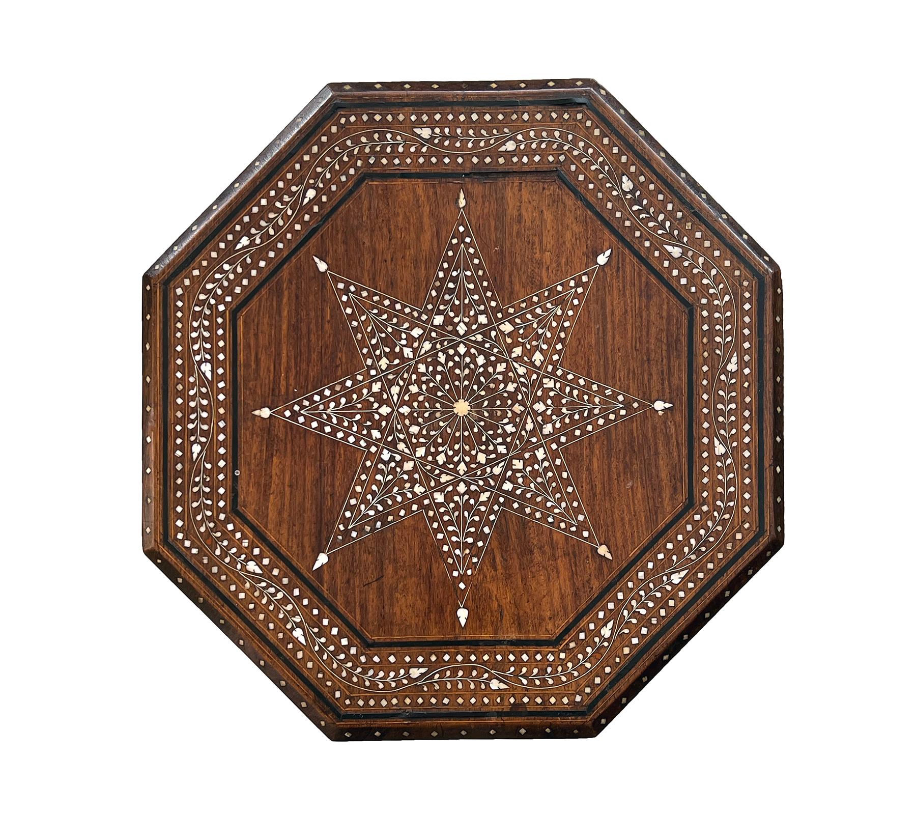 originally used as traveling tea tables for the British in India; the octagonal top with central eight-pointed star medallion within a perimeter band depicting a meandering foliate vine ; raised on a hinged base with arabesque spandrels