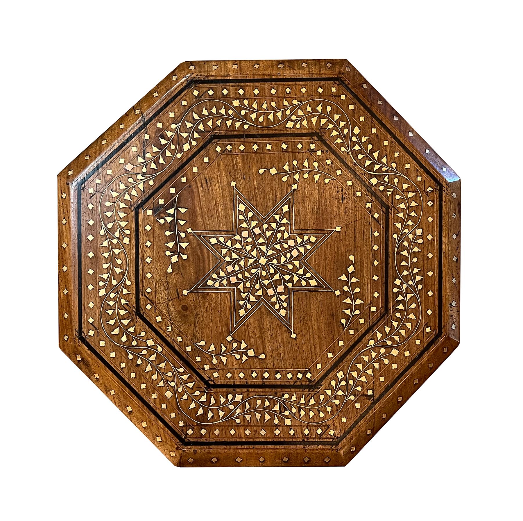 originally used as traveling tea tables for the British soldiers in India; the octagonal top with central star medallion surrounded by inlaid meandering foliate vines; raised on a hinged base with arabesque spandrels