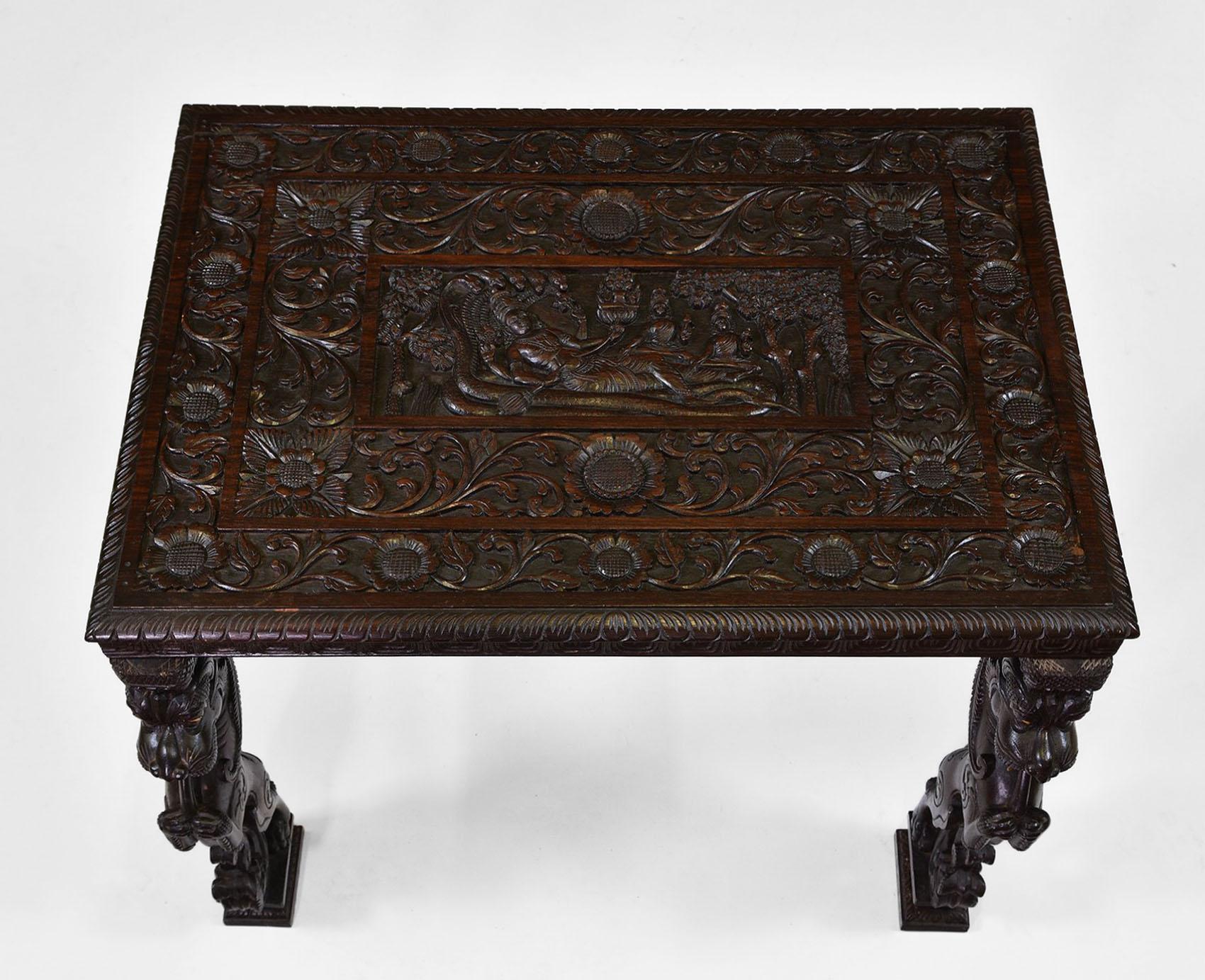 A wonderful profusely carved Padouk wood Anglo Indian occasional table with mythical lions to each leg and bone fangs. It boasts intricate floral decoration and carved top depicting Vishnu. Circa 1900.

The table has been waxed. The legs screw on,