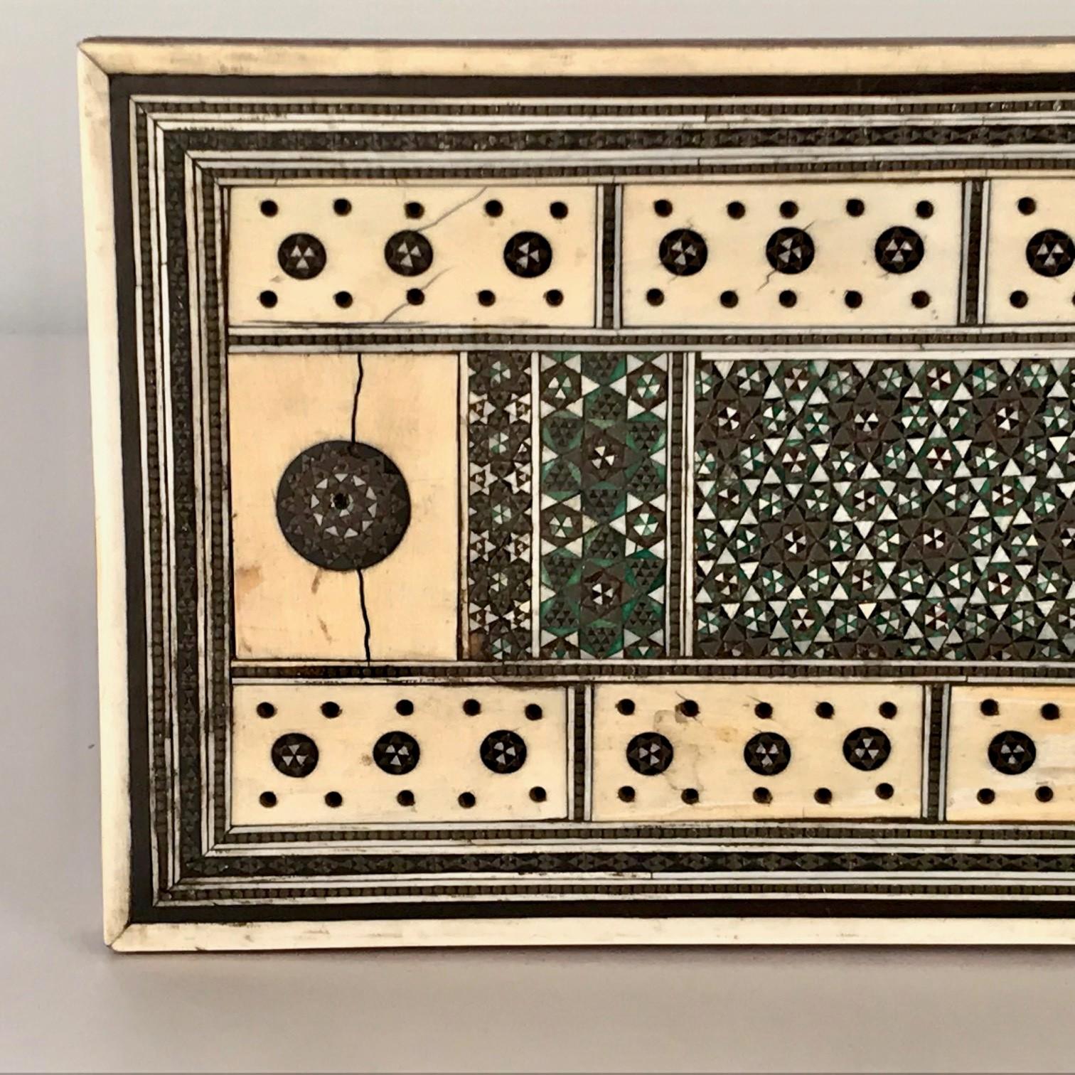 This board is sandalwood and is intricately inlaid with geometric marquetry and ebonised lines as well as the pierced oblong panels required for the game. the back is set with an old lightly worn velvet panel.