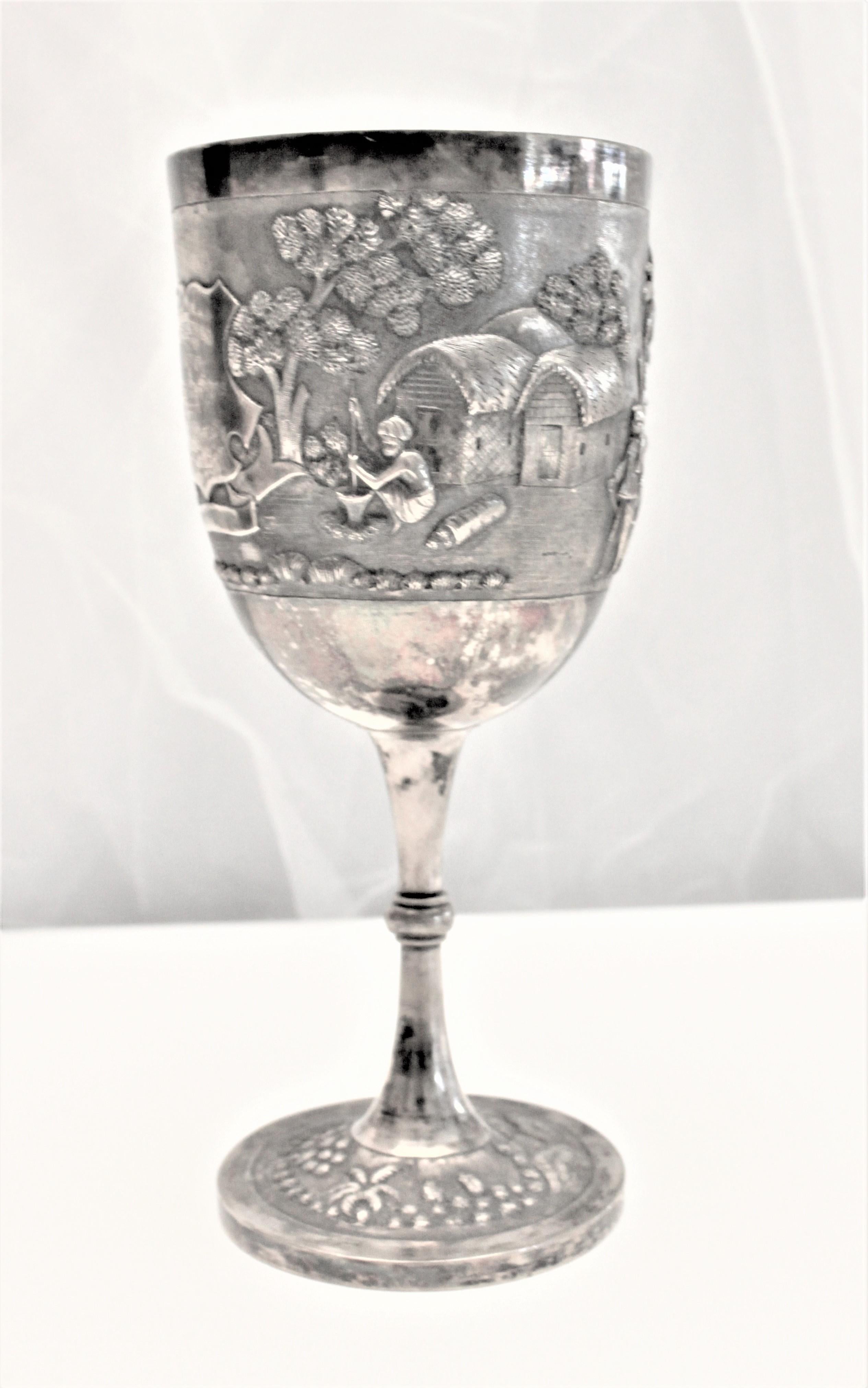 Presumed to have been made in India in the early 20th century, this solid silver trophy goblet is very ornately decorated in the Anglo-Indian style in a combination of repousse and chased work depicting village life. The shield on the front is
