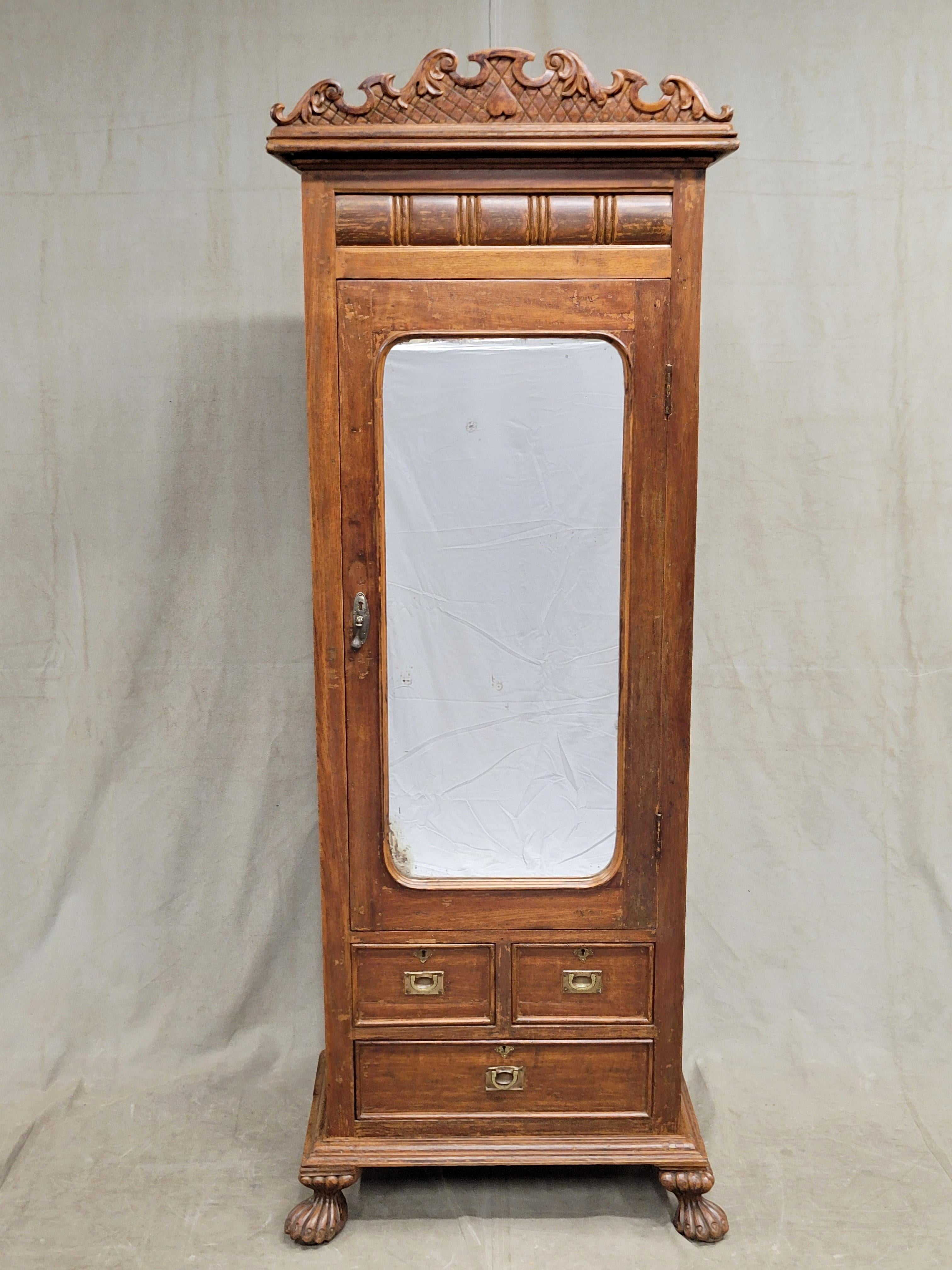 A sweet antique (late 1800s or early 1900s) Anglo-Indian teak petite armoire cupboard with mirror. A hand carved curvilinear crown, oversized paw feet, and overall small scale give this piece such unique flair. Campaign brass pulls accent the