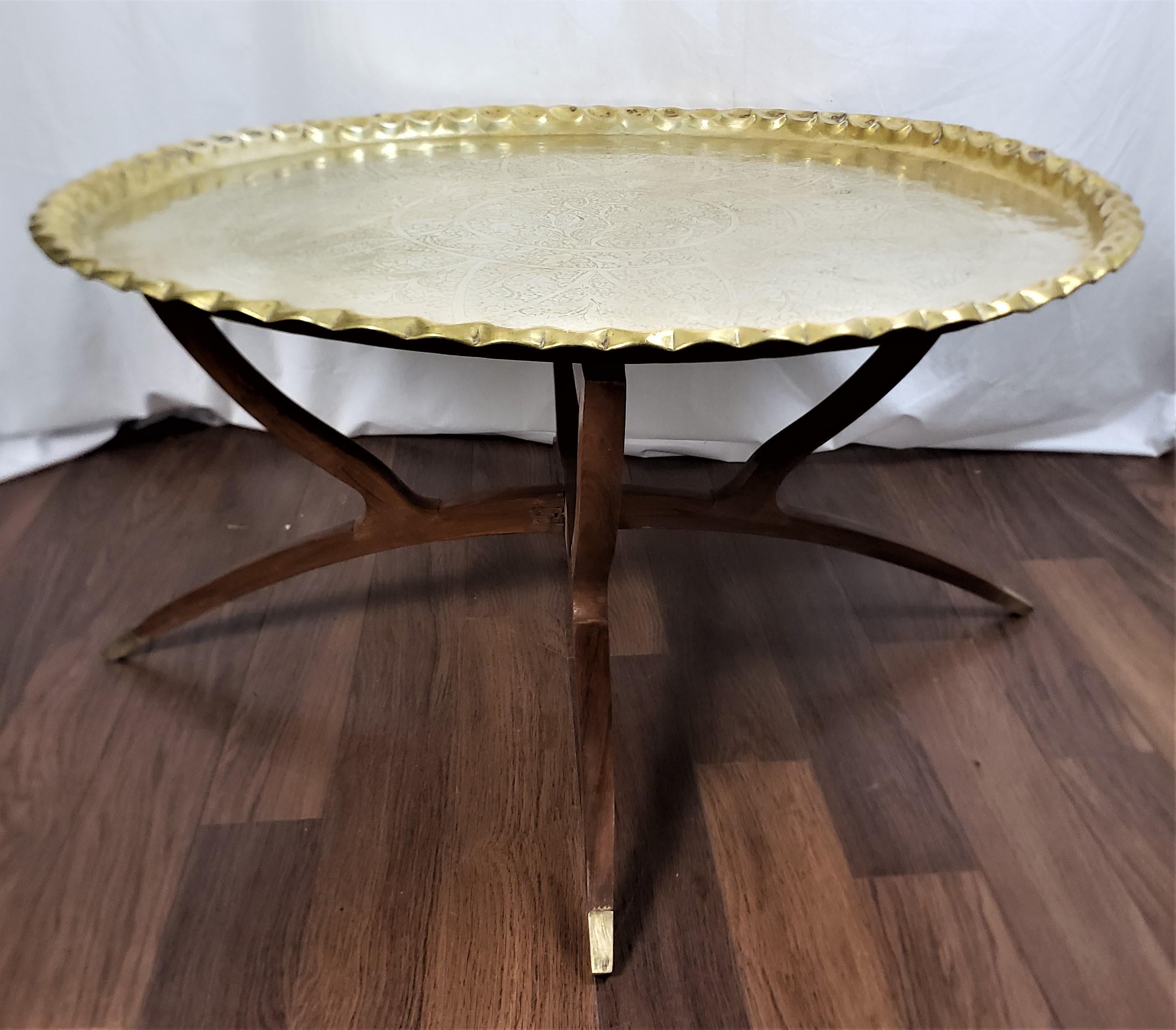 This antique tray table is unsigned, but presumed to have originated from India and date to approximately 1920 and done in the period Angro-Indian style. The hand-crafted tray is composed of brass with an engraved medallion in the center, and a