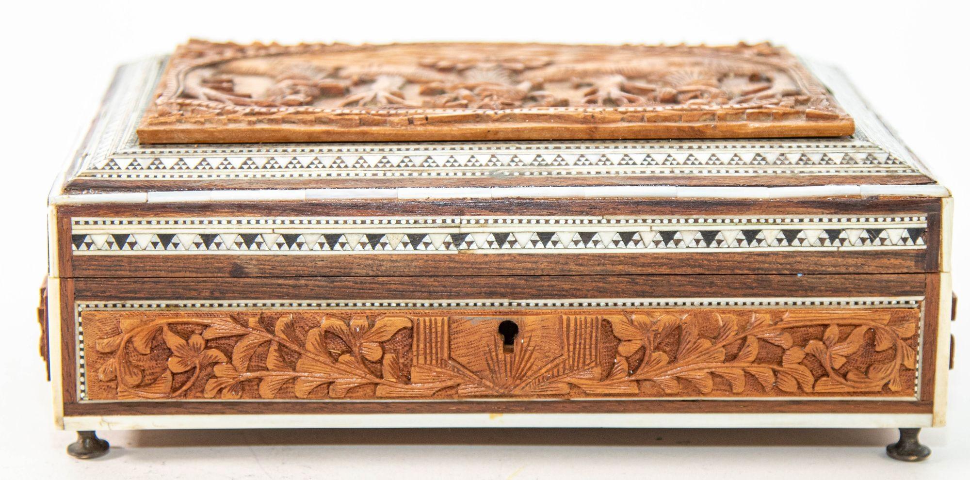 Antique 19th century Anglo-Indian jewelry, trinket footed box, inlay with ebony, mosaic marquetry Sadeli work and a carved Hindu scene on top.
The box case is made from sandalwood with highly hand-carved padouk wood reliefs on all sides and banded