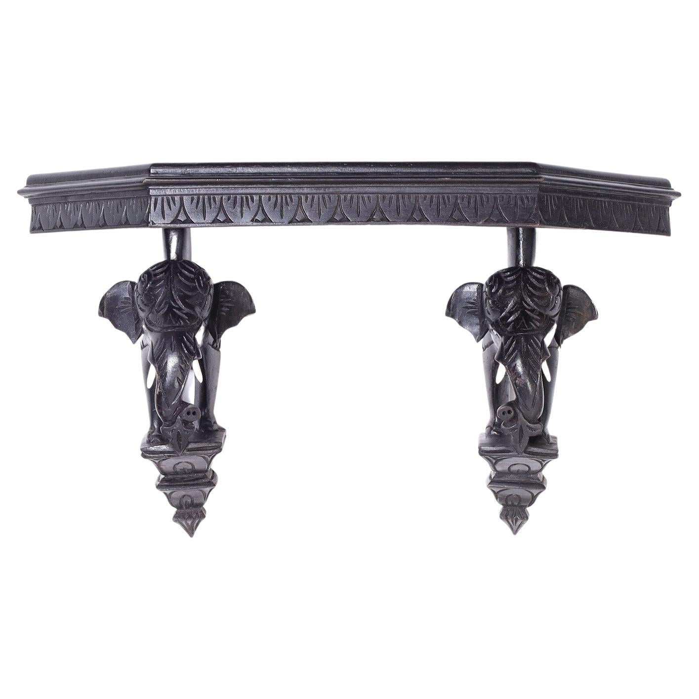 Intrigante console murale ou étagère coloniale britannique sculptée dans du bois dur indigène avec une finition ébénisée et présentant une paire de supports d'éléphants sur des plateformes.