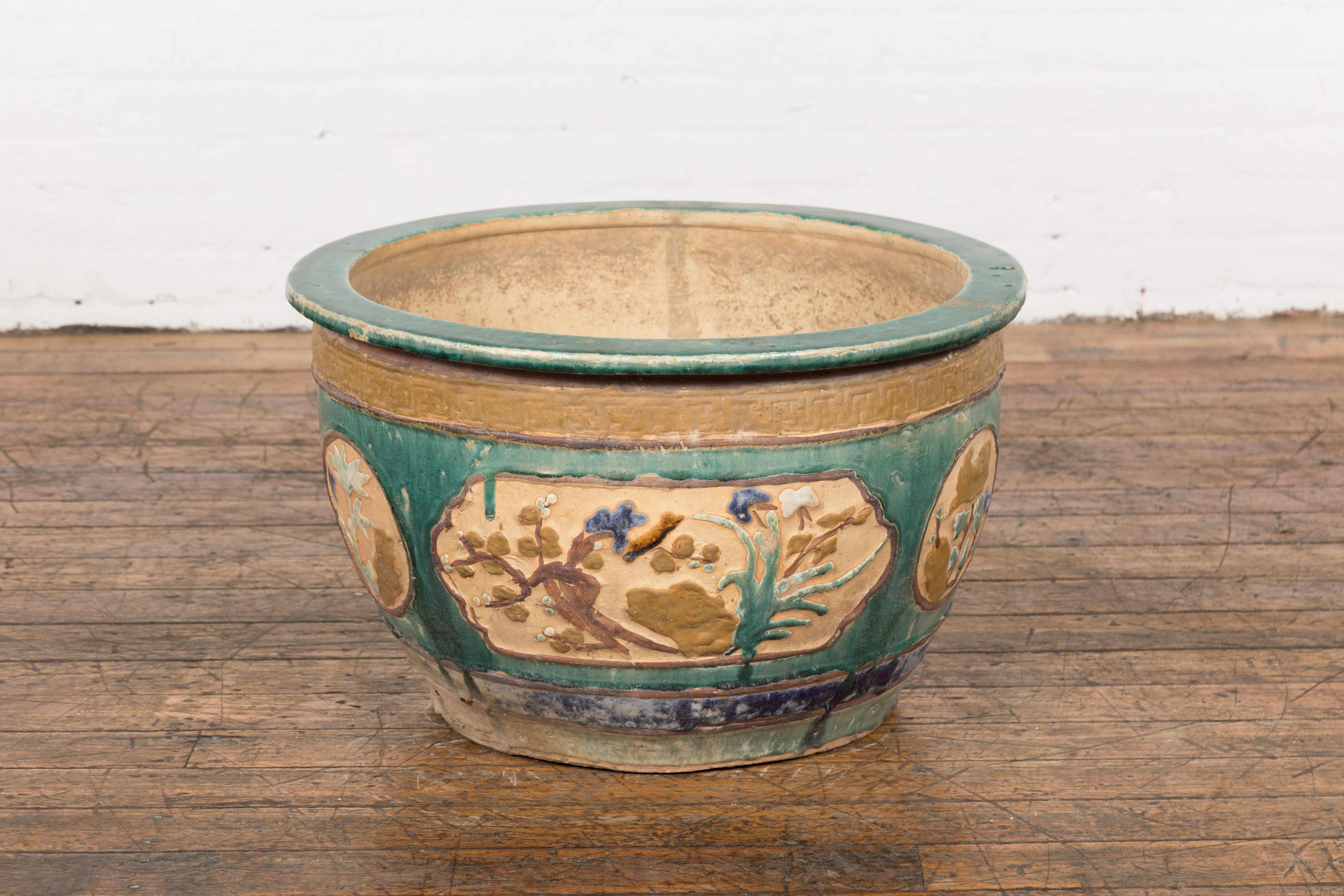 An antique 19th century Annamese green, blue and ocher planter from Vietnam with trees ], foliage, flowers and bird motifs as well as distressed patina. Handcrafted in Vietnam during the 19th century, this planter features a circular silhouette