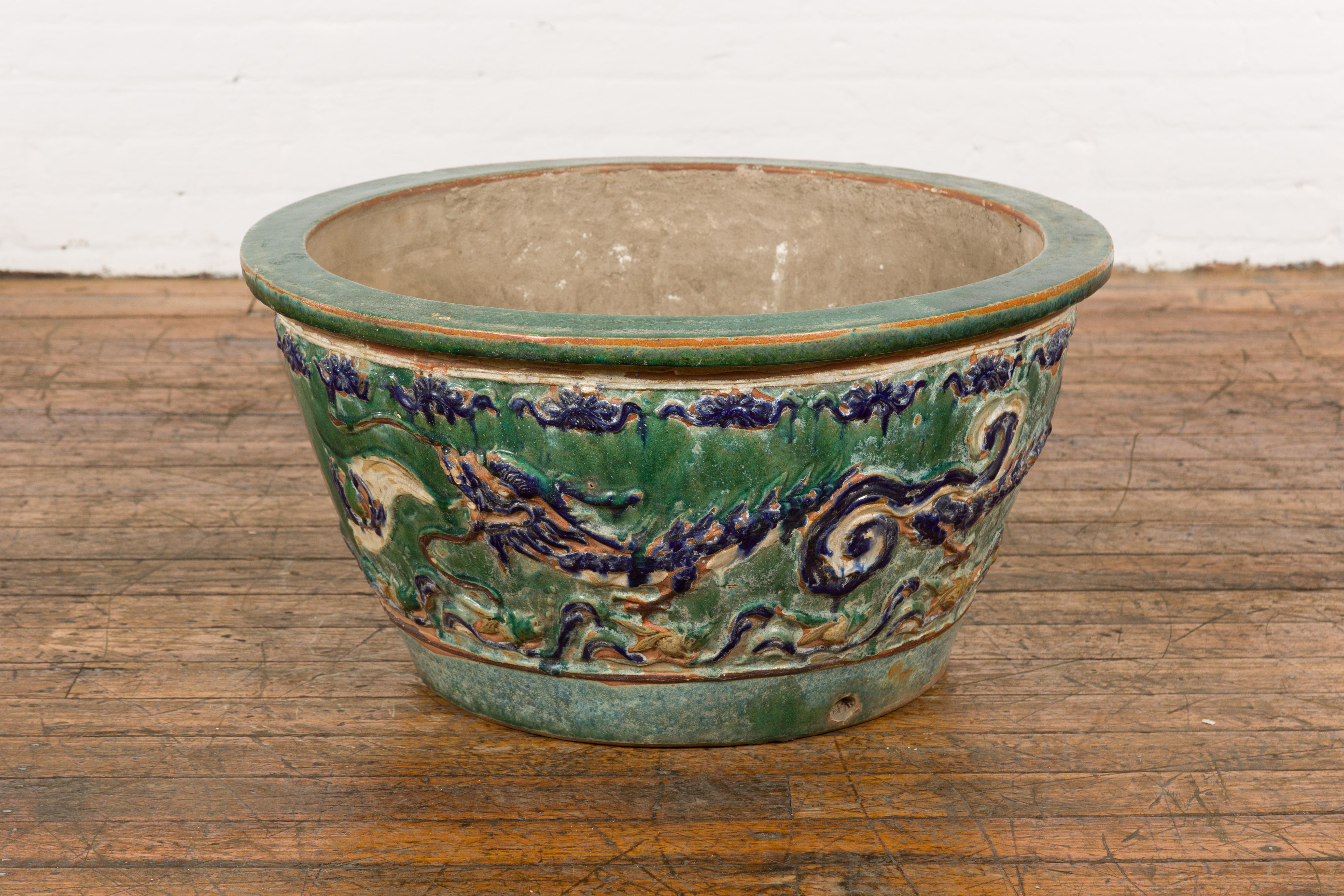 An antique 19th century Annamese green and blue planter from Vietnam with dragon, female figure, large scrolling clouds, foliage, distressed patina and petite evacuation hole in the front. Introducing a captivating piece from the 19th century, this