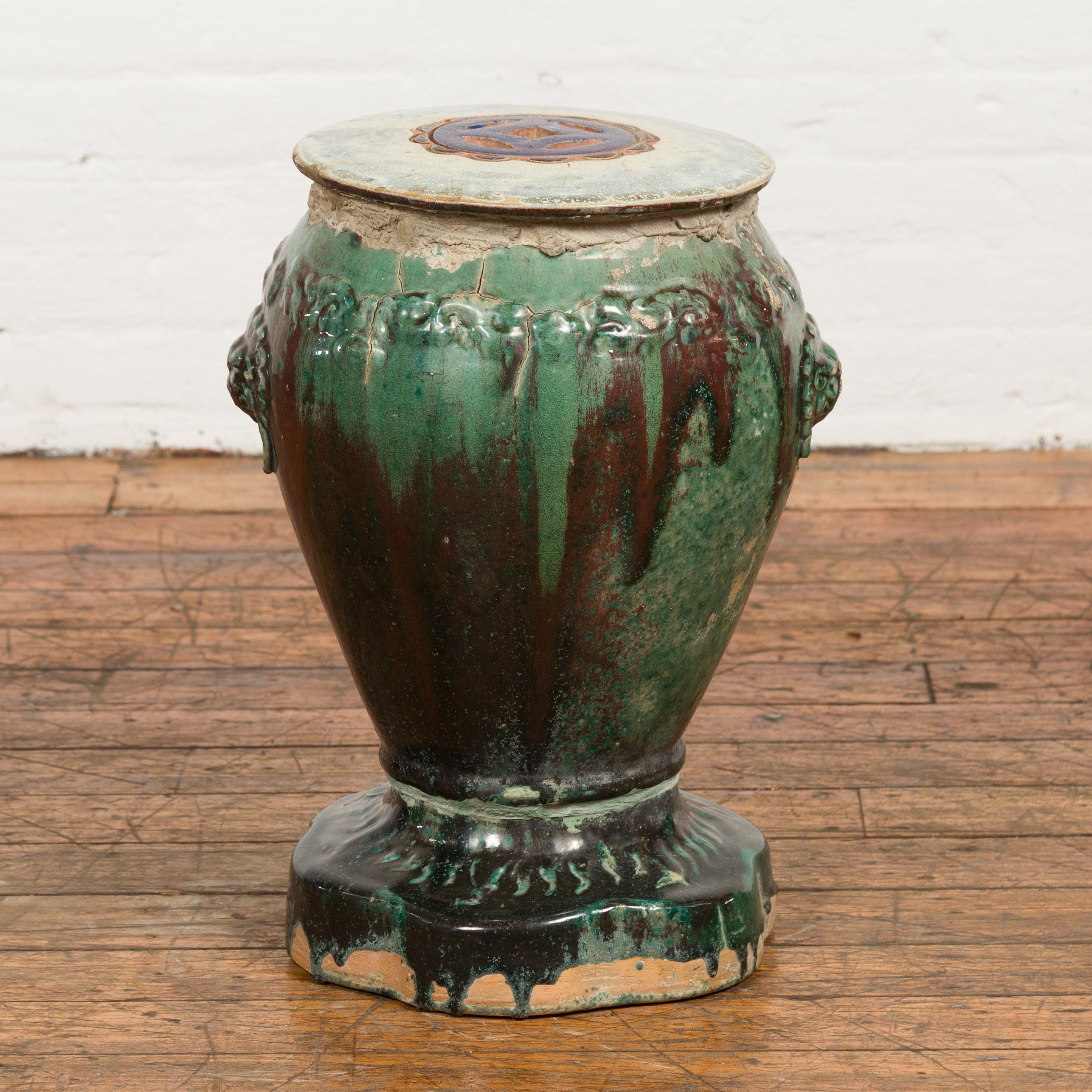 An antique 18th or 19th century Annamese ceramic garden seat from Vietnam with green and brown glaze, raised scrolling frieze, pierced top, guardian lion handles and shaped base. Made of ceramic and boasting a green glaze accented beautifully with