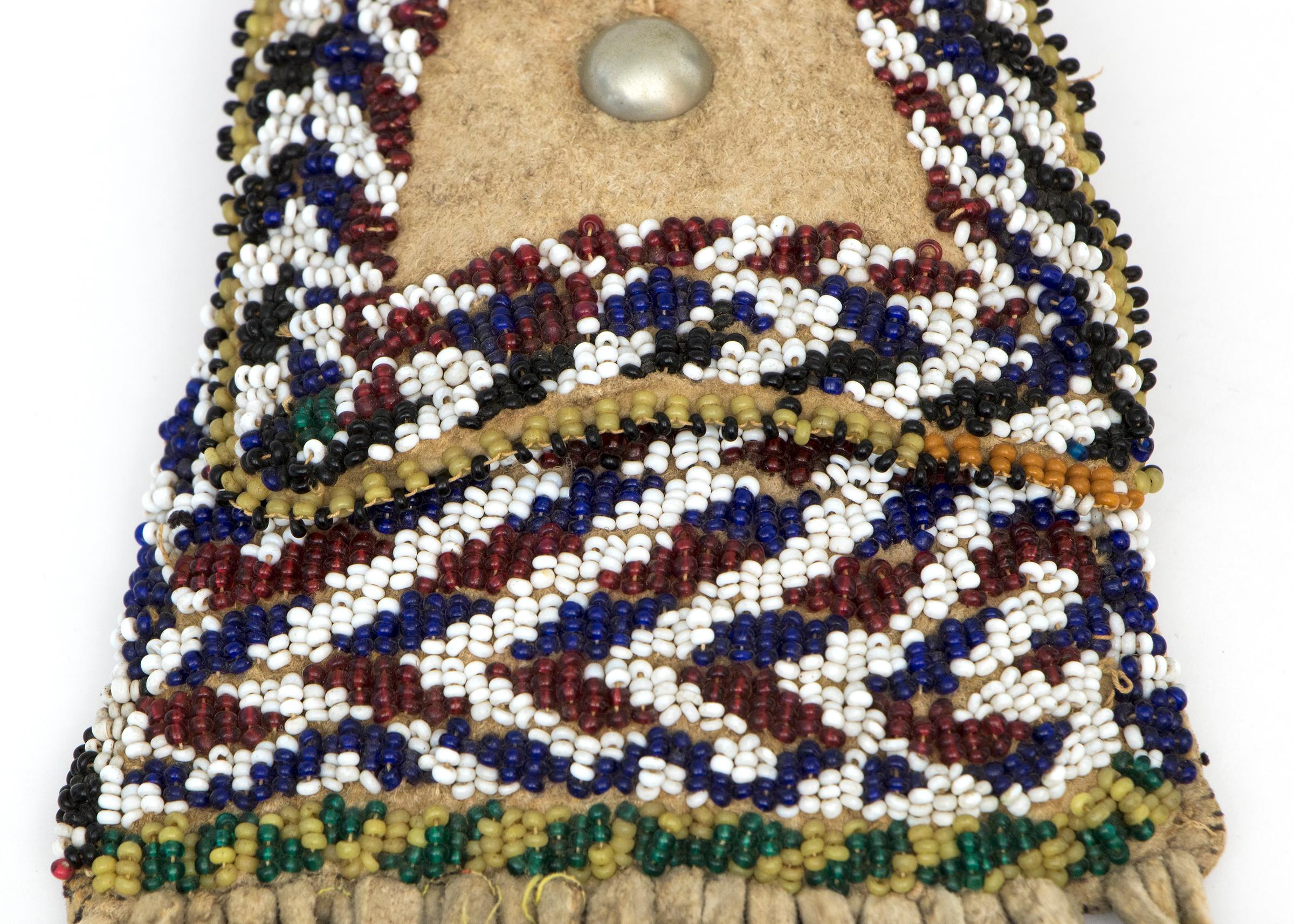 Vintage Apache (North American Indian) 19th century Strike-A-Lite Pouch. Constructed of native tanned Mule Deer hide and beaded with trade beads, fringed with pony beads and tin-cone danglers, a German silver button adorns the flap. Overall