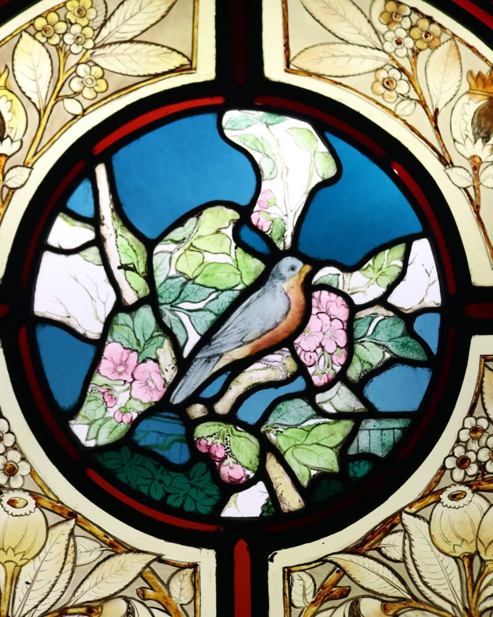 An antique arched stained glass window attractively decorated with a bird, possibly a nuthatch, and fruiting foliage surrounded by a panel of stylised roses and thorns. This beautiful window dates from the late 19th century yet it’s vibrant colours