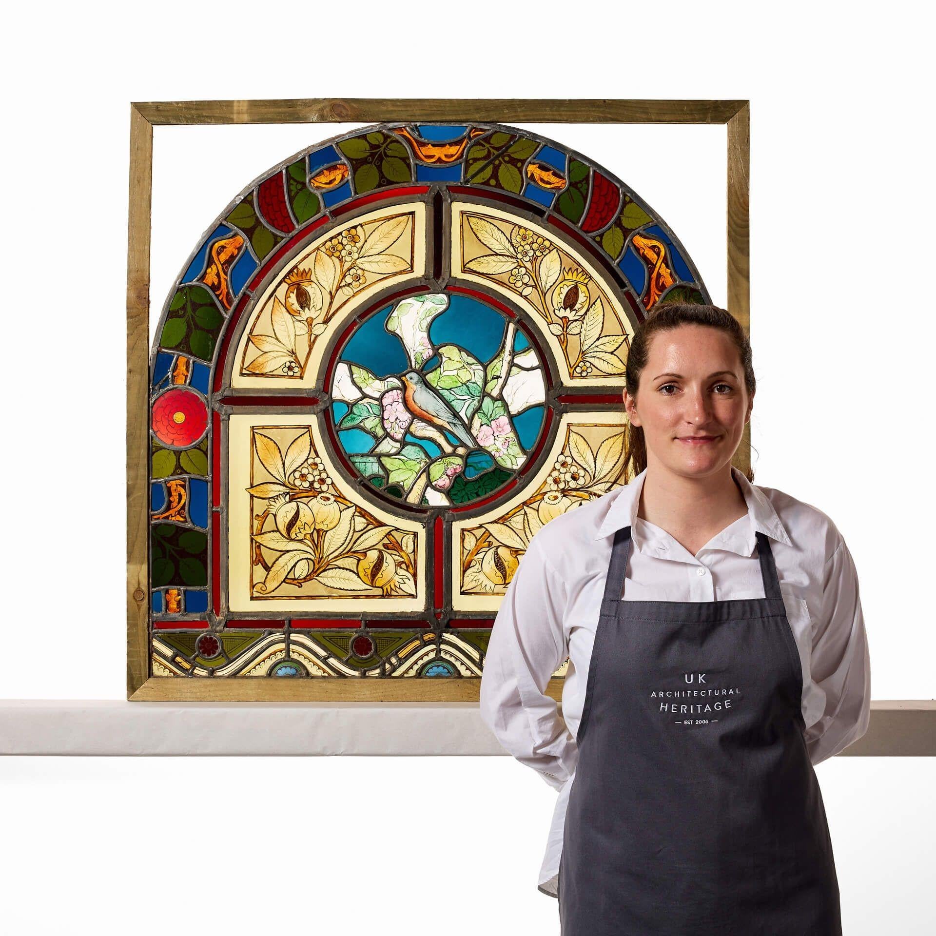 An antique arched stained glass window attractively decorated with a bird, possibly a nuthatch, and fruiting foliage surrounded by a panel of stylised roses and thorns. This beautiful window dates from the late 19th century yet it’s vibrant colours