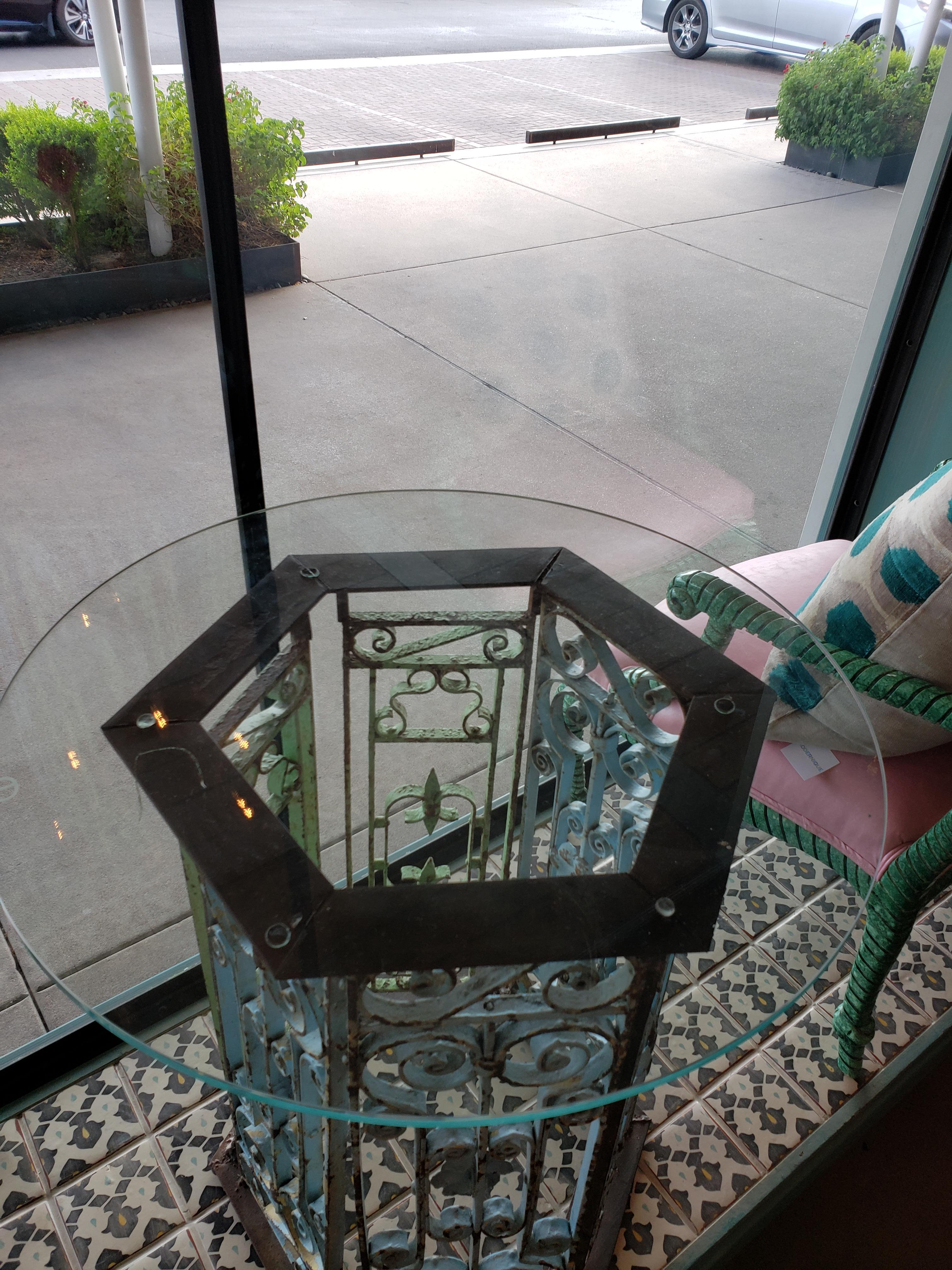 This table base is constructed of iron fragments found in New Orleans. They most probably were from a staircase. The colors are of turquoise and green. The glass top accompanies the base for a stunning and unique entry, side or cafe