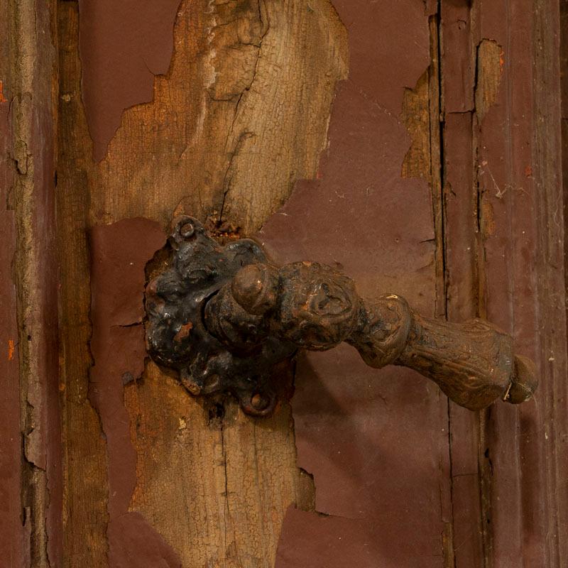 These massive, heavily paneled doors are even more impressive in person. The original red paint is chipped and distressed, adding to the authentic vintage nature of this pair of salvaged exterior doors. The aged paint may easily be stripped, taking