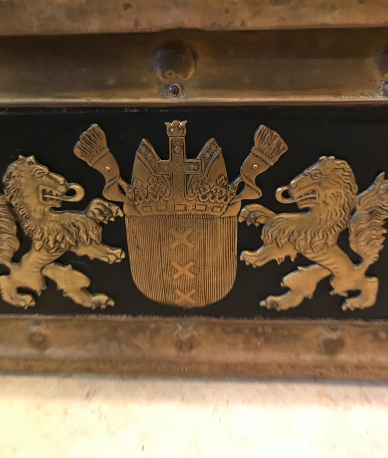 Antique wood trunk adorned with coat of arms on the top and front sides.
Brass trimmed with studs and on castors.