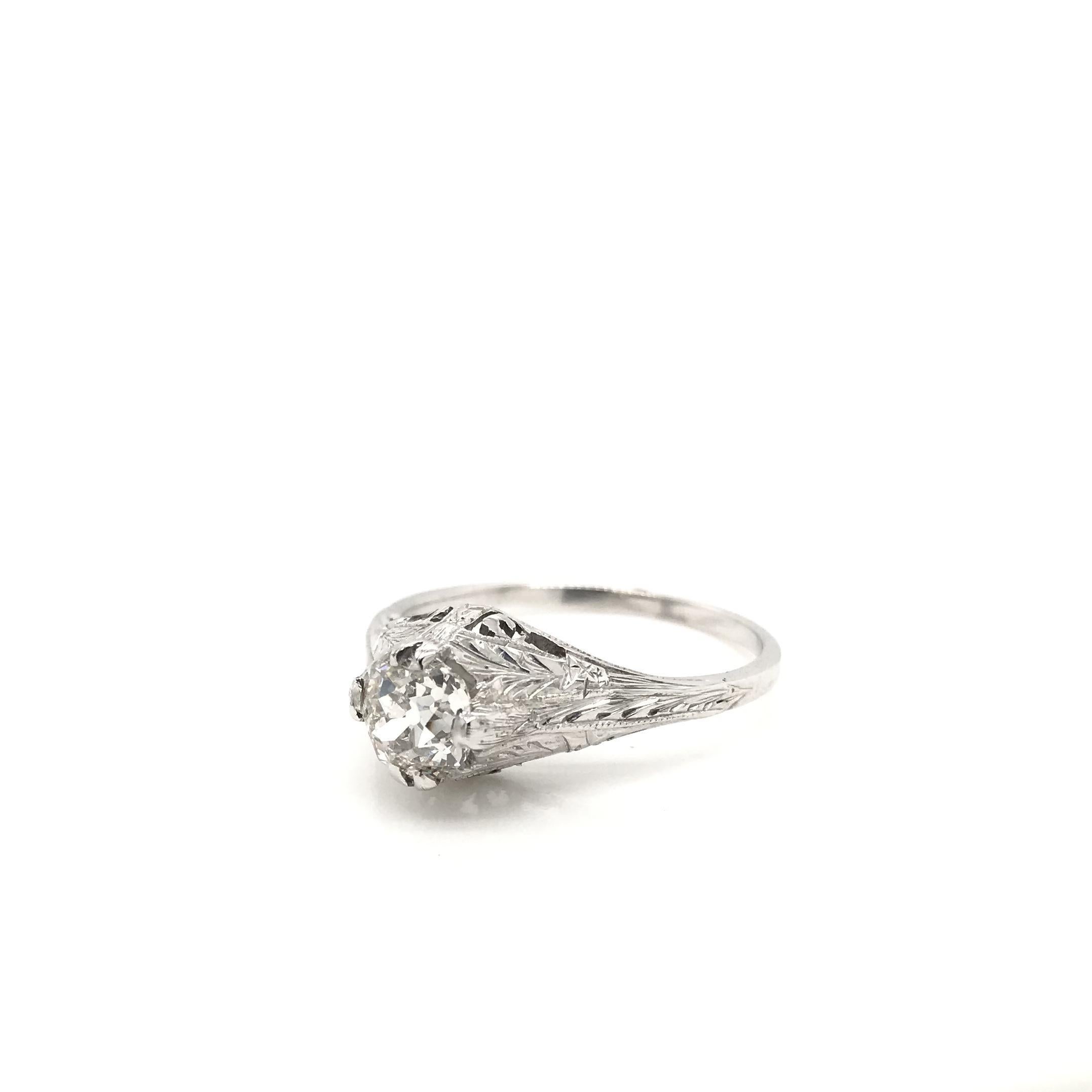 This antique diamond solitaire style ring was crafted sometime during the Art Deco design period (1920-1940). The setting is 20K white gold and features a center diamond measuring approximately 0.71 carats. The center diamond is an antique Old