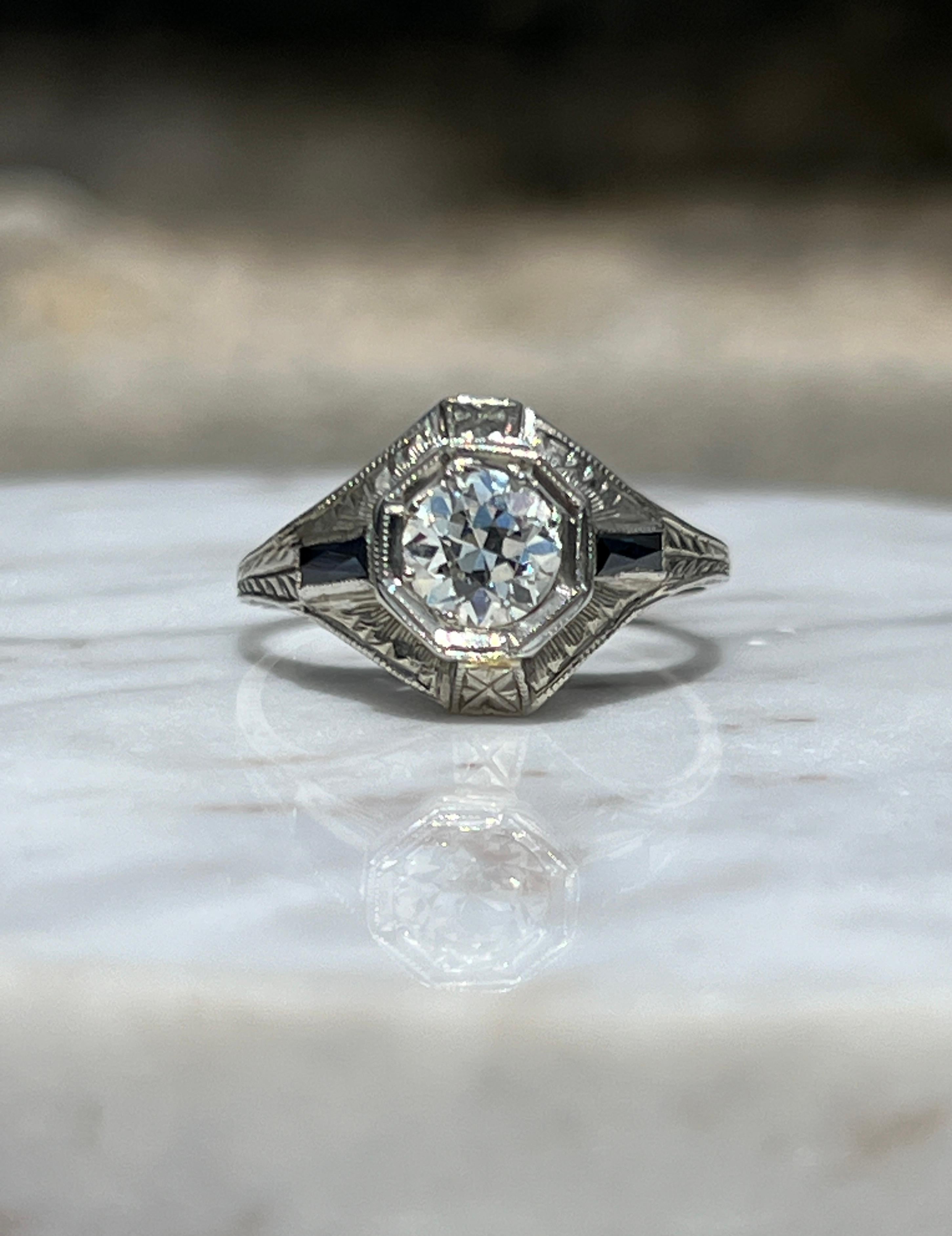 This romantic Art Deco engagement ring, crafted from 18 karat white gold, features a hand-engraved design that beautifully showcases an old European cut diamond of approximately 0.80 carats, with I color and VS2 clarity. The diamond is elegantly