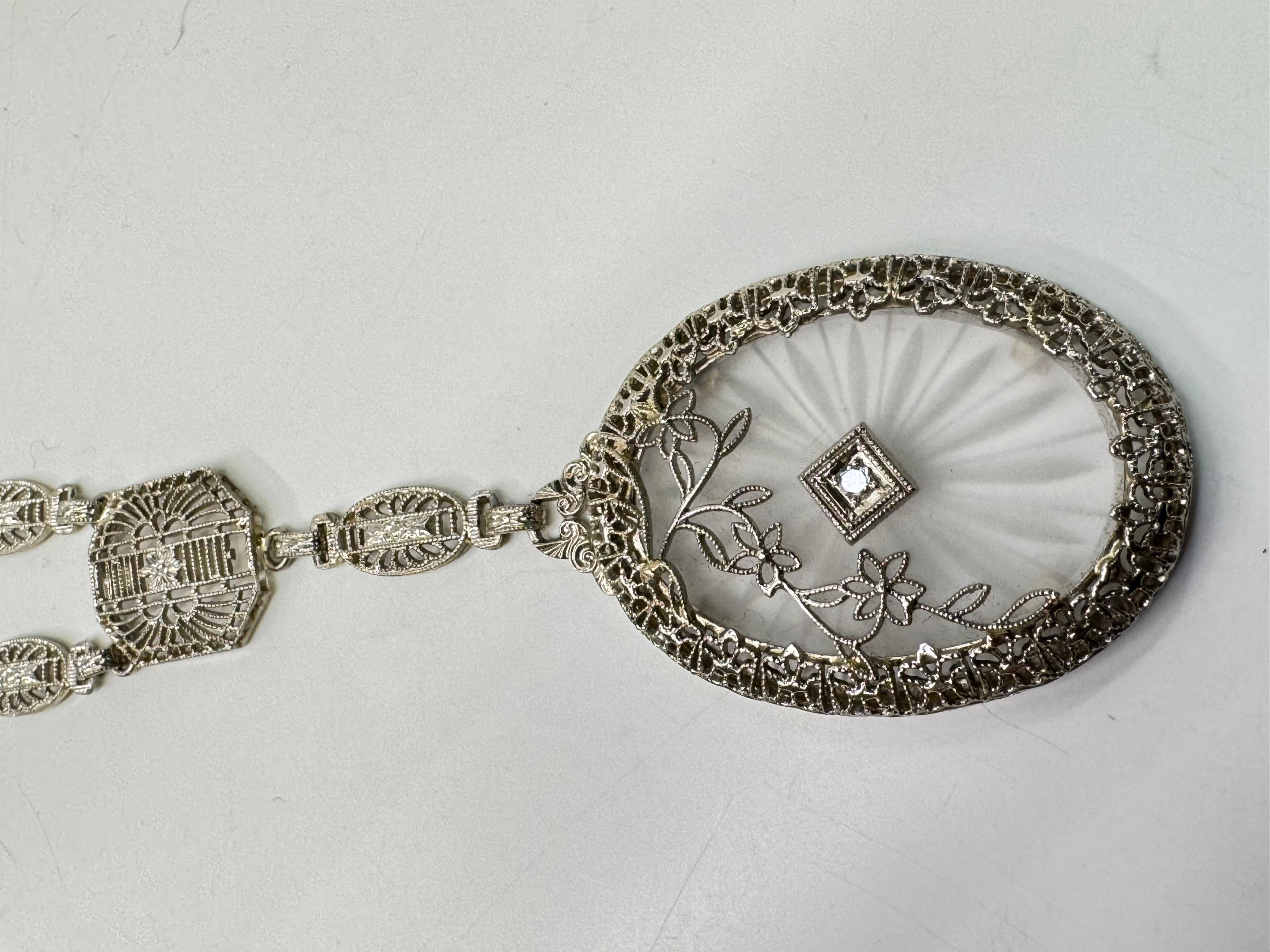 This exquisite antique Art Deco pendant necklace is a true testament to early 20th-century craftsmanship. Made from solid 14k white gold, it features an elegant oval-shaped camphor glass panel with intricate etching designs, evoking the delicate
