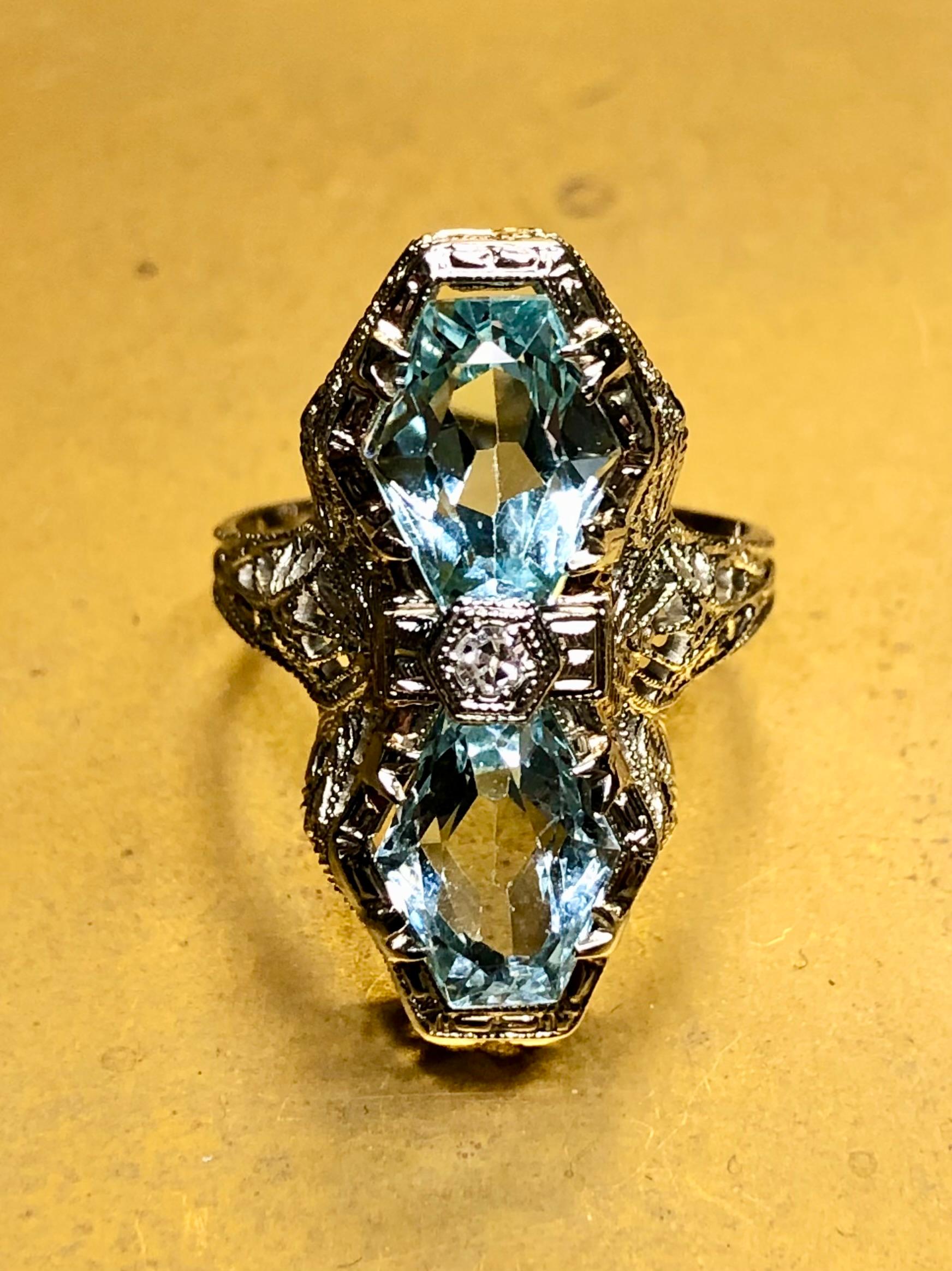 An original Art Deco north /south filigree cocktail ring done in intricately worked 14K white gold and set with two matching kite shaped natural aquamarines with a small old cut diamond in the center. Total aquamarine weight is approximately