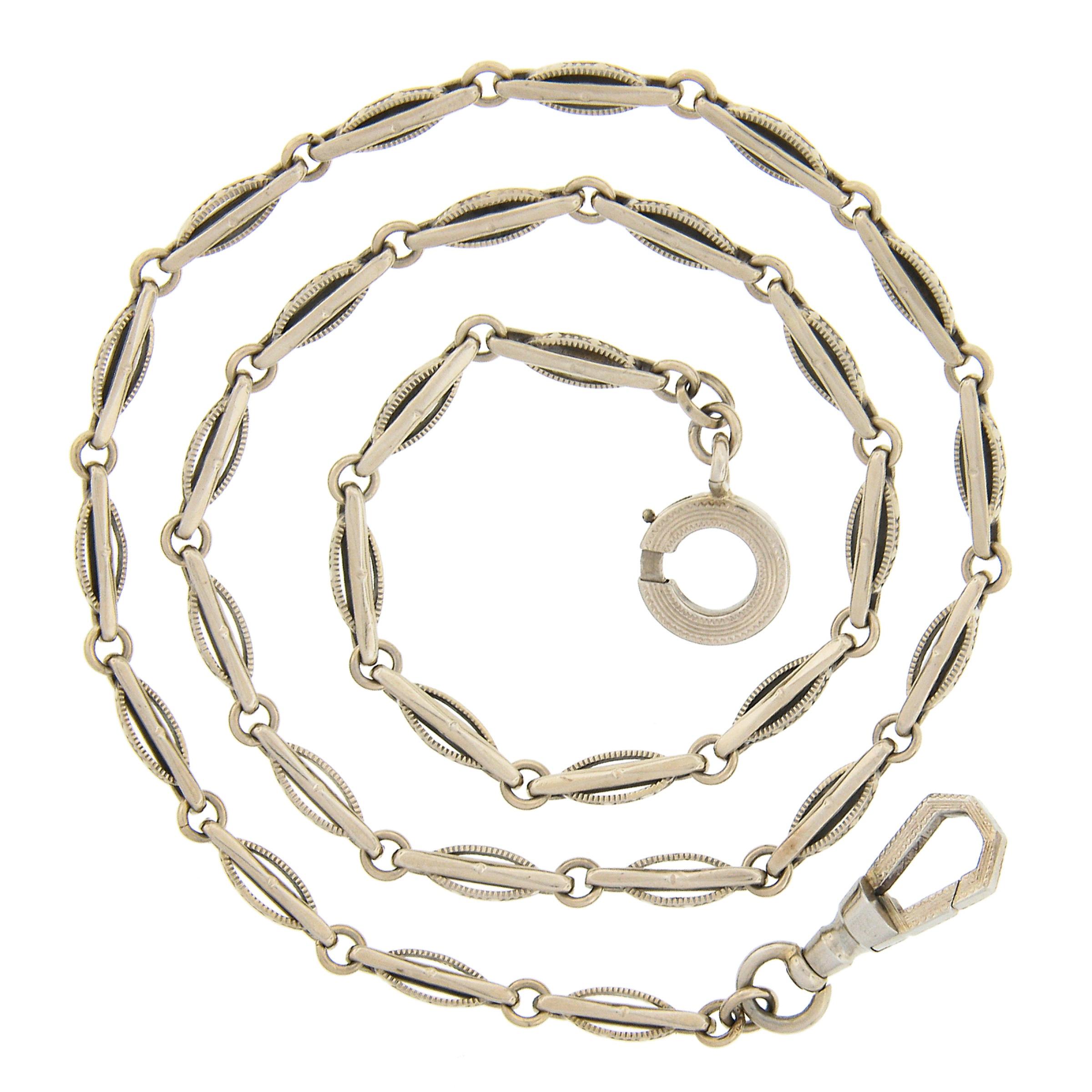This beautiful antique art deco pocket watch chain was crafted from solid 14k White gold. It features delicate polished bars on uniquely etched ornate oval links. The chain measures 16 inches in length and is secured with a detailed & textured large