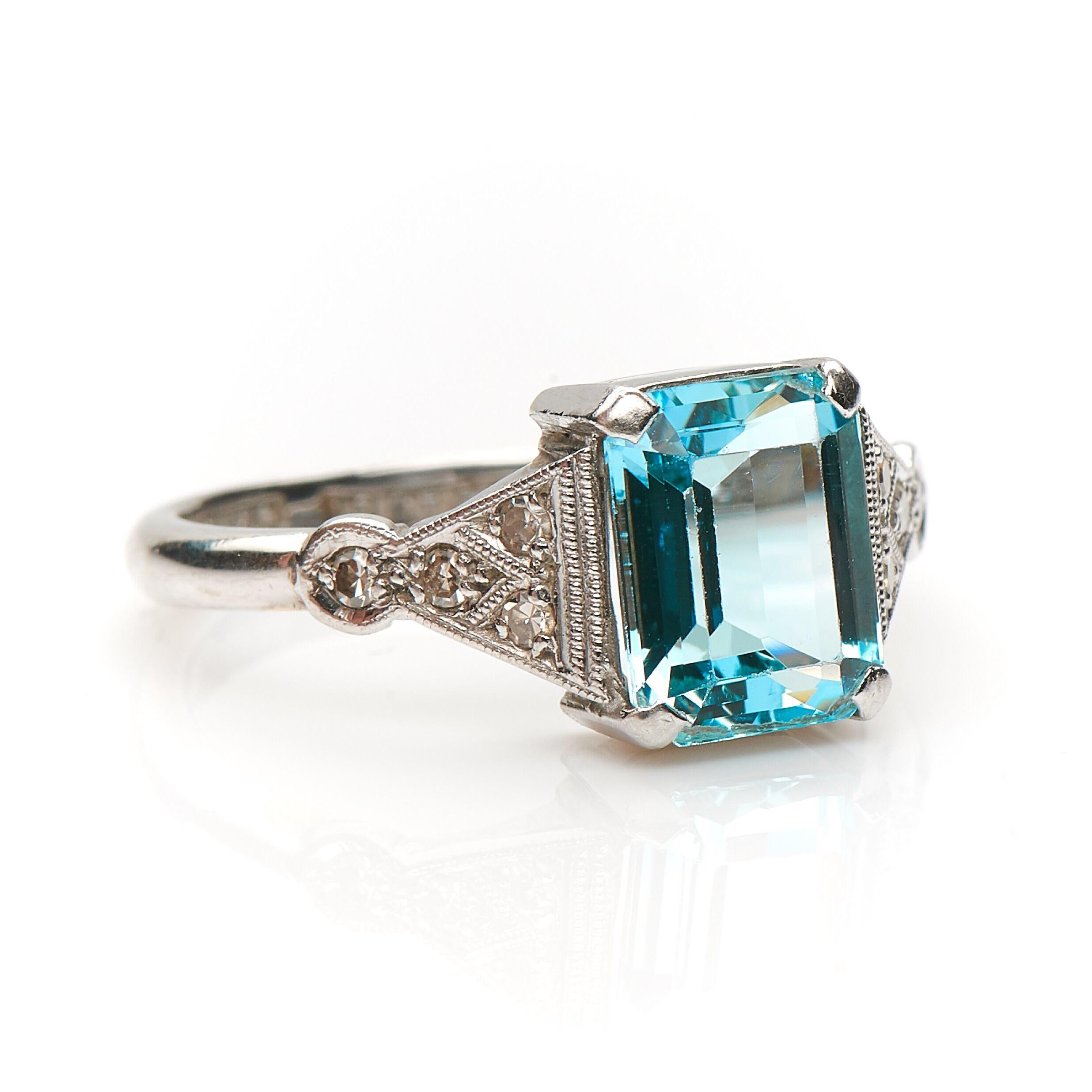 Art Deco, aquamarine and diamond ring, circa 1930. Set to centre a step-cut aquamarine flanked by trumpeting diamond set shoulders all finely finished with millegrain boarders. The aquamarine is a very pretty hue of blue, it creates a beautiful