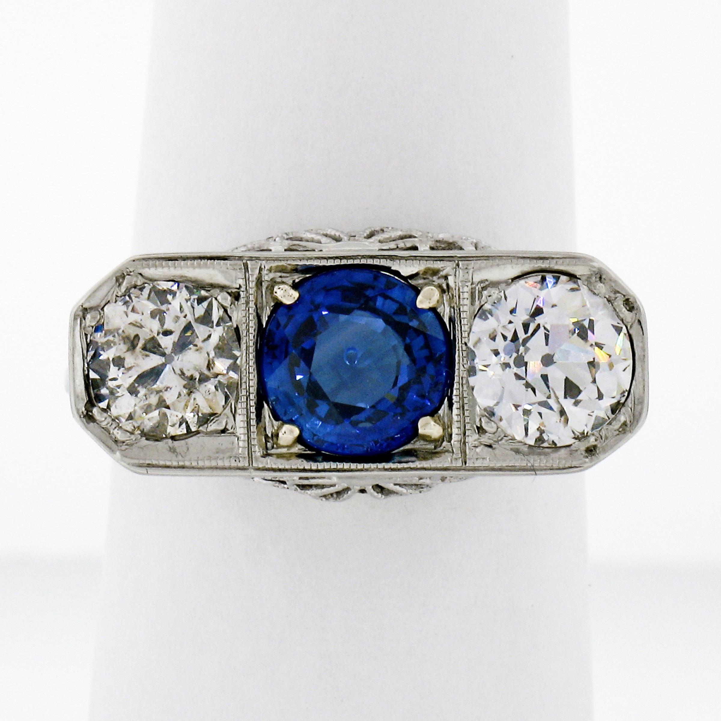 This gorgeous, all original antique three stone ring was crafted in solid 18k white gold during the art deco period and features a stunning, GIA certified, 1.55 carat round brilliant cut natural sapphire stone. The sapphire displays the richest and