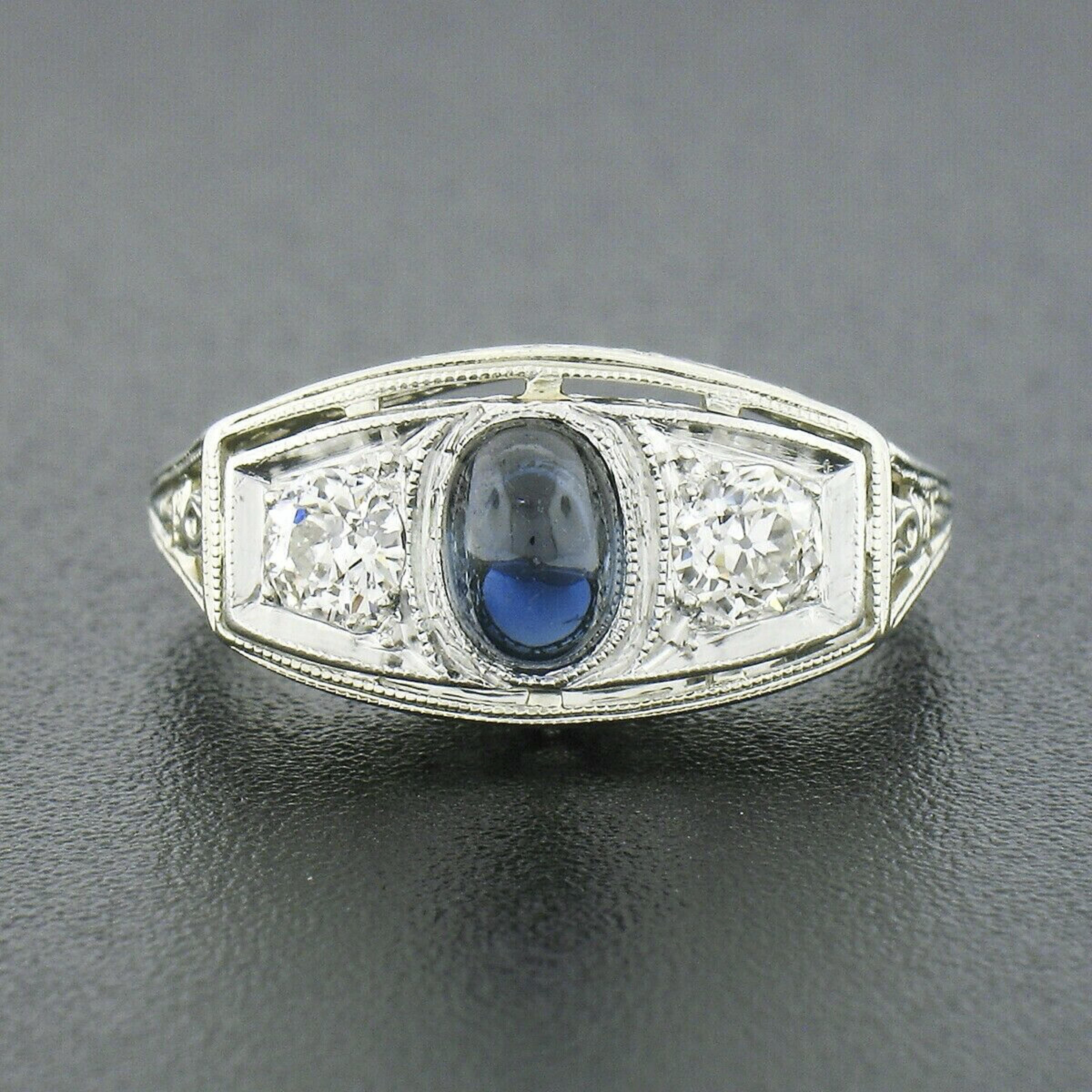 This beautiful antique ring was crafted in solid 18k white gold with a solid platinum top during the art deco period. This three stone style ring features a high oval cabochon cut sapphire neatly bezel set at its center and flanked on both sides