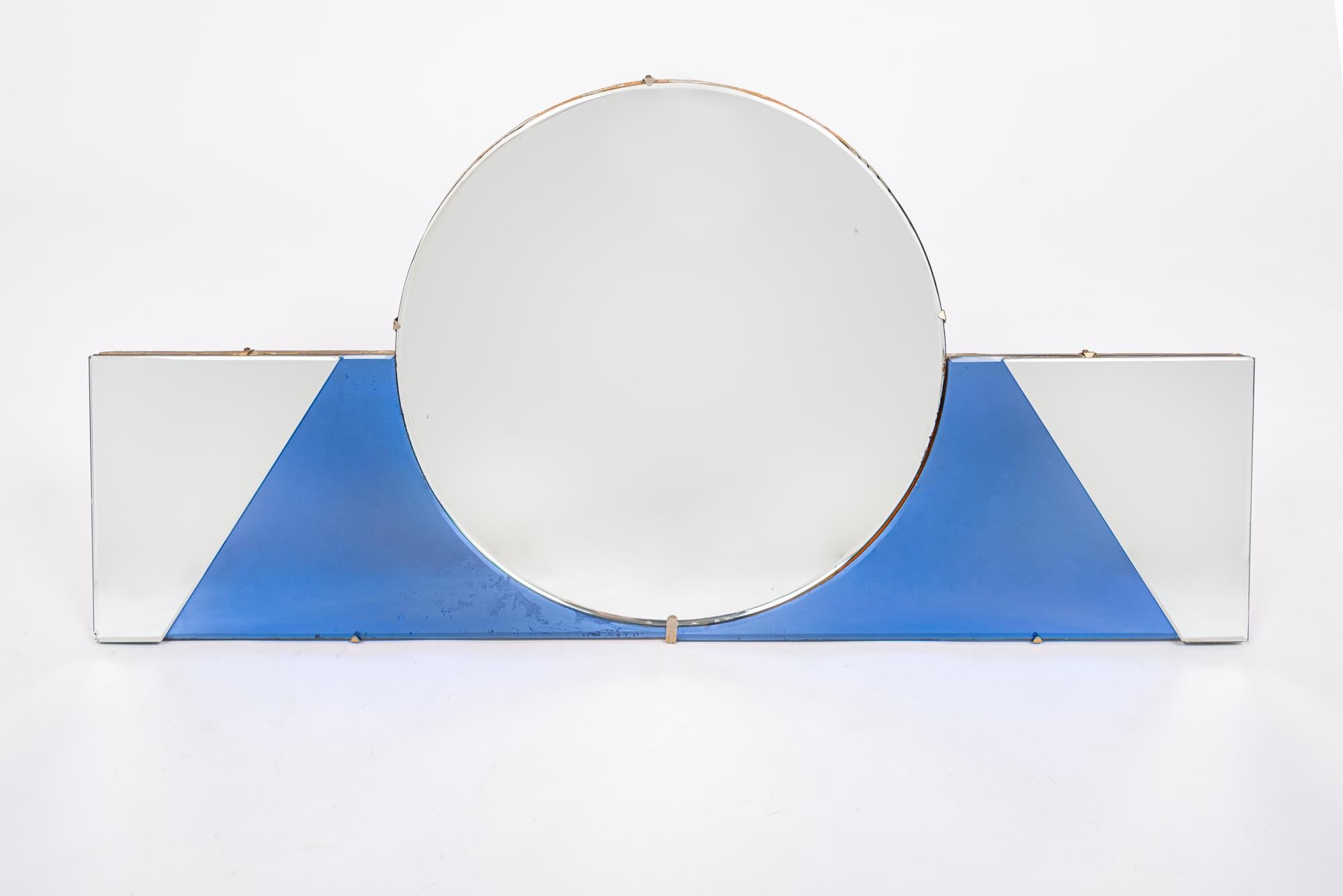 This beautiful antique Art Deco hanging beveled wall mirror is circa 1930. The mirror has an elegant, geometric design featuring a center round mirror over a rectangular lower band with a colored blue glass field. Hanging wire on wooden backside