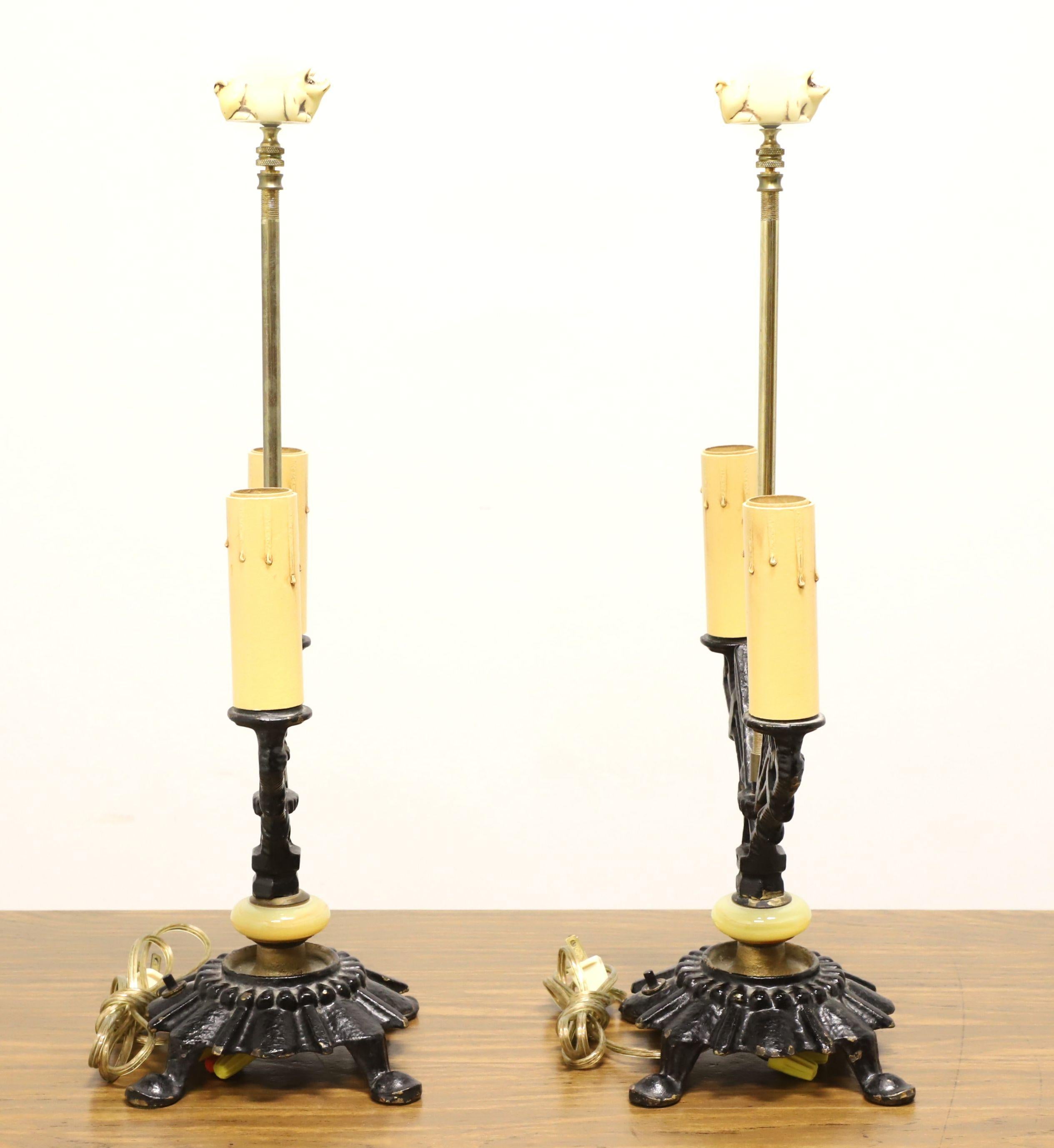 A pair of Art Deco style dual light table lamps, unbranded. Made of black painted metal in a uniquely designed dual candlestick shape, cream colored plastic bulb socket with faux dripped wax to give appearance of a candle, decorative cream color